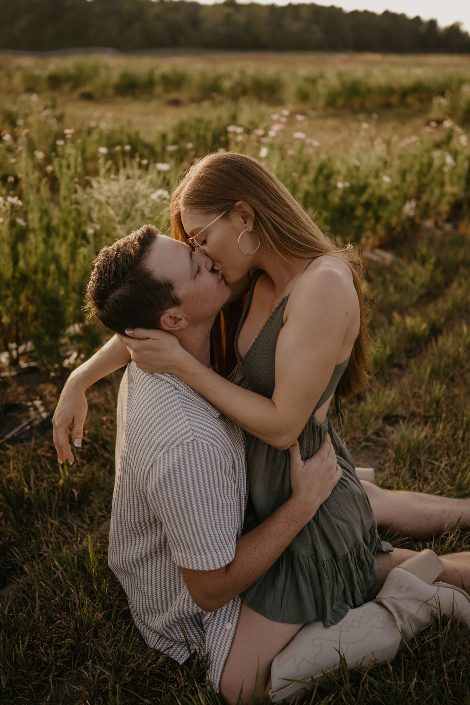 Couple sharing a passionate kiss while sitting in a wildflower meadow during warm sunset light.