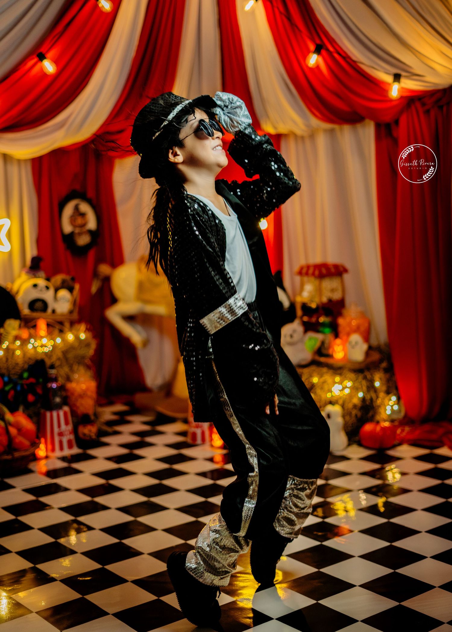 Kid in Michael Jackson costume with sequin jacket and fedora strikes dramatic pose on checkered floor.