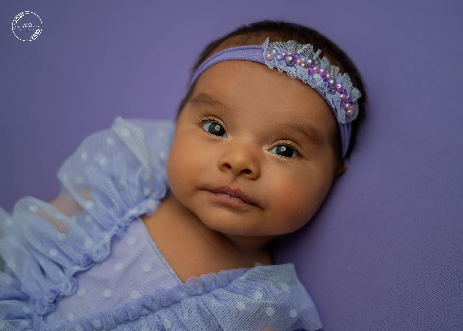 Beautiful baby girl in purple polka dot outfit wearing lavender floral headband.