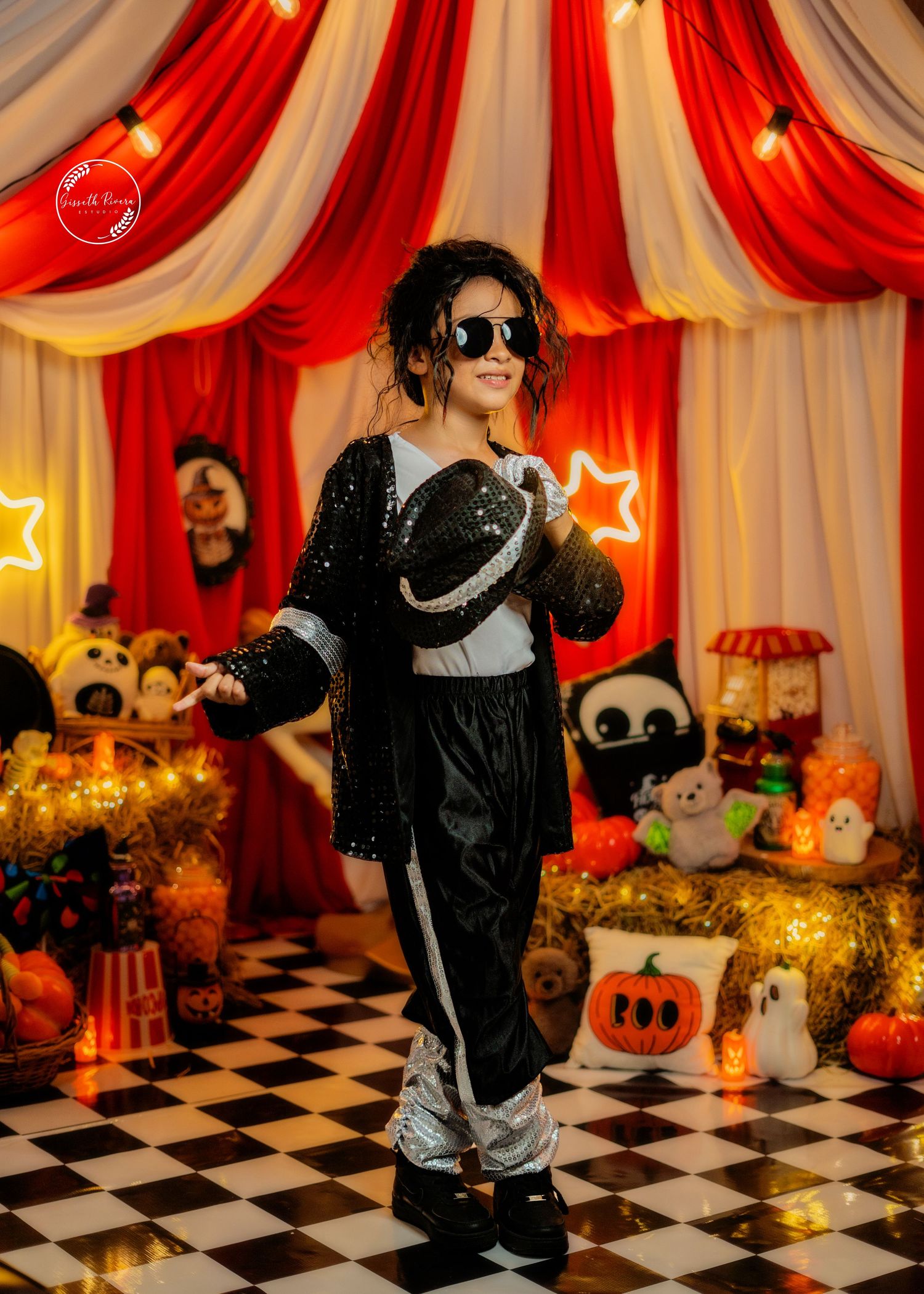 Child dressed as Michael Jackson in sequin jacket and hat poses in festive Halloween circus backdrop.