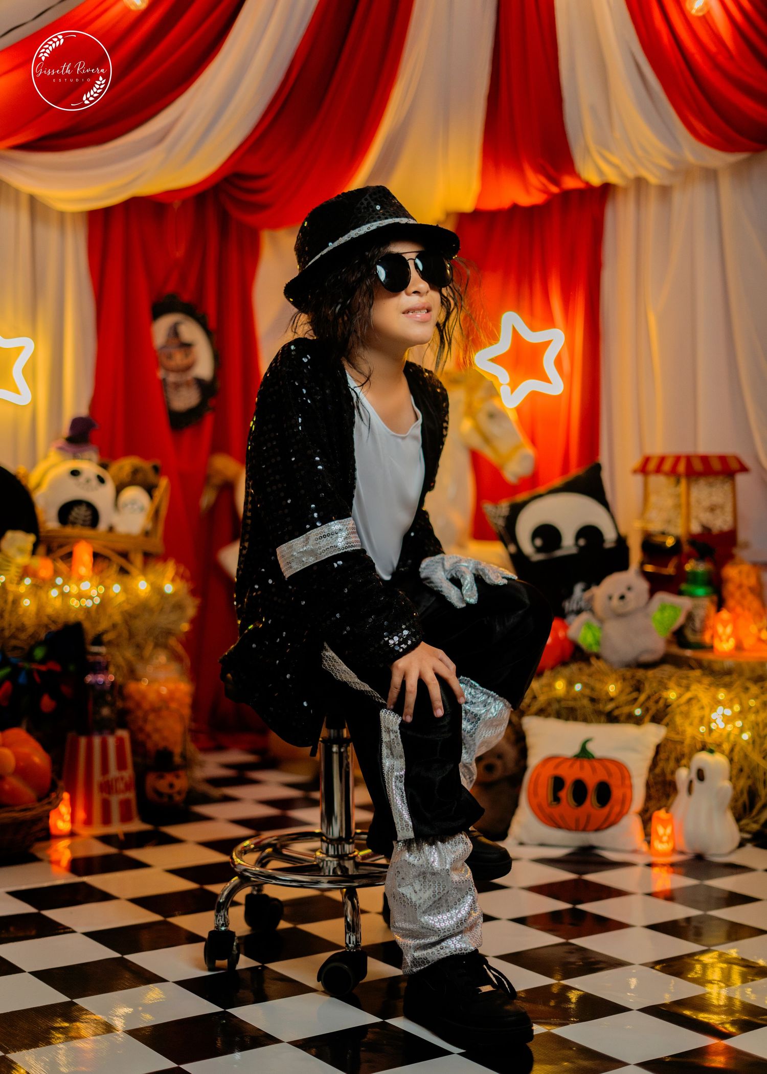 Child in Michael Jackson sequin outfit sits on stool in Halloween circus themed photo studio.