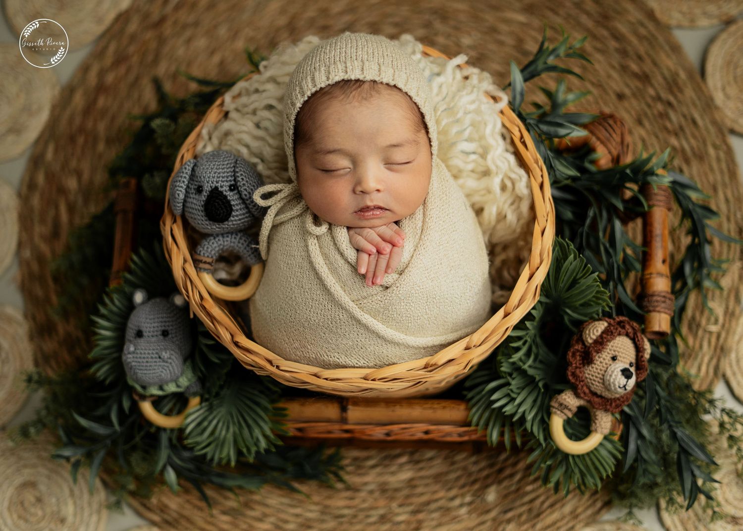 Sleeping newborn wrapped in cream swaddle inside wicker basket with knit bonnet and stuffed animal toys.