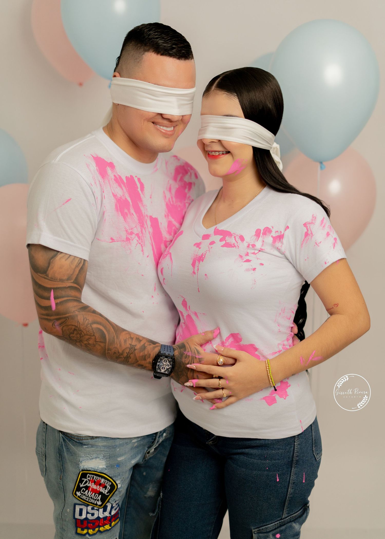 Gender reveal photo with blindfolded couple covered in pink paint with balloons in background.