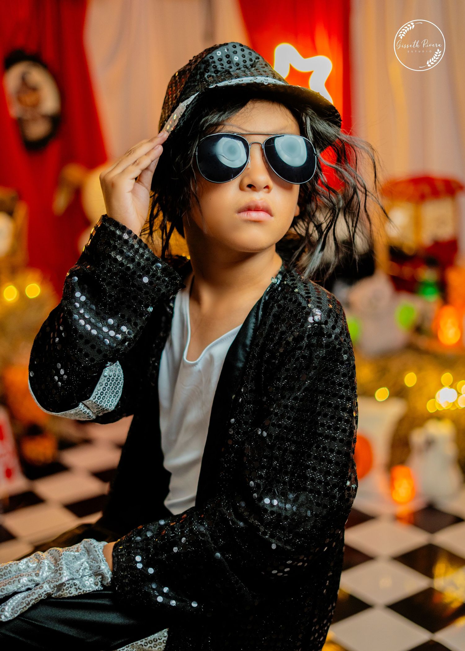 Close-up of child in Michael Jackson sequin jacket and oversized sunglasses adjusting black fedora hat.