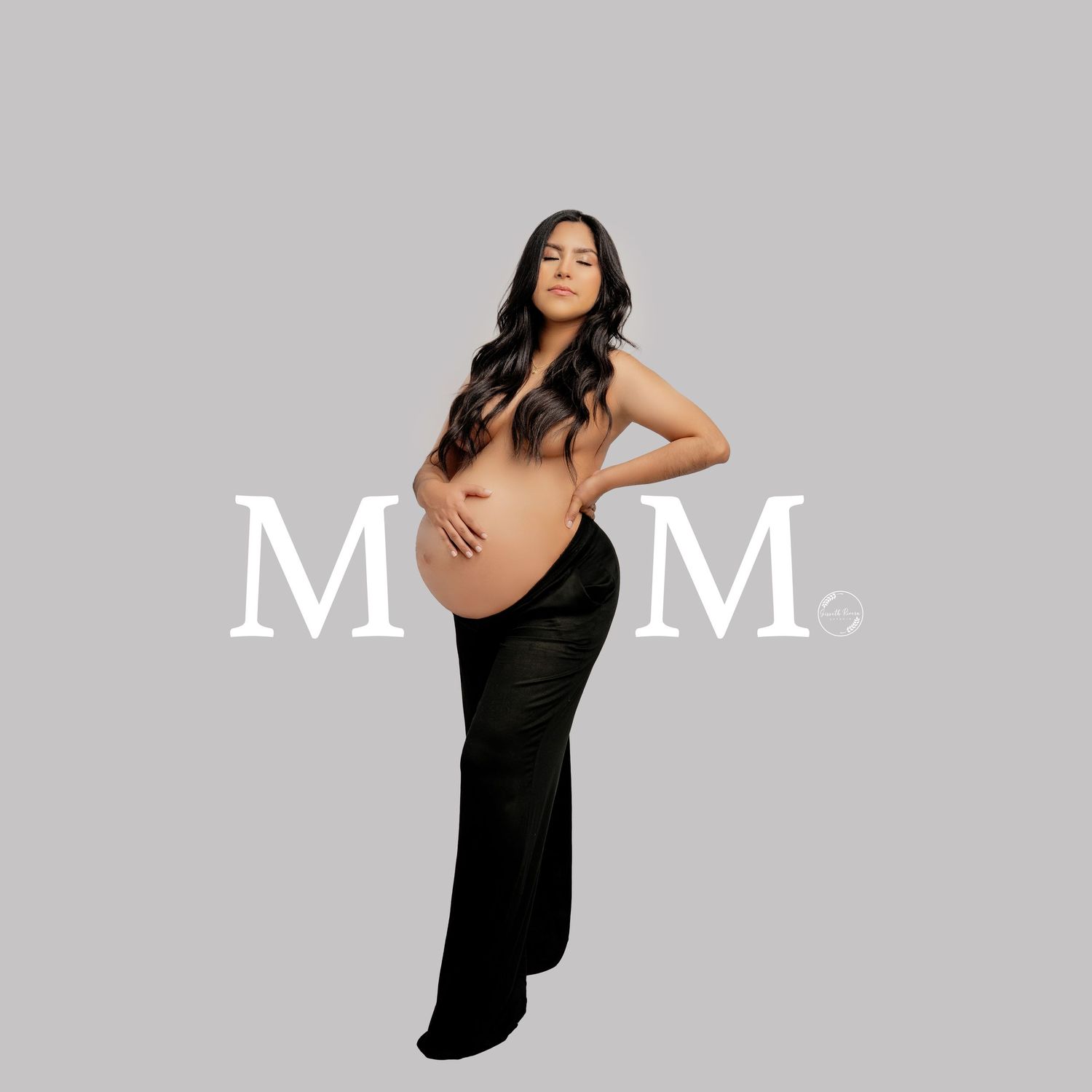 Pregnant woman in black skirt posing topless with MOM text overlay on gray background.