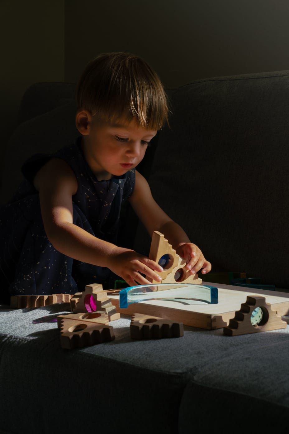 Toddler playing with wooden building blocks on the sofa, illuminated by a strip of natural sunlight at home.