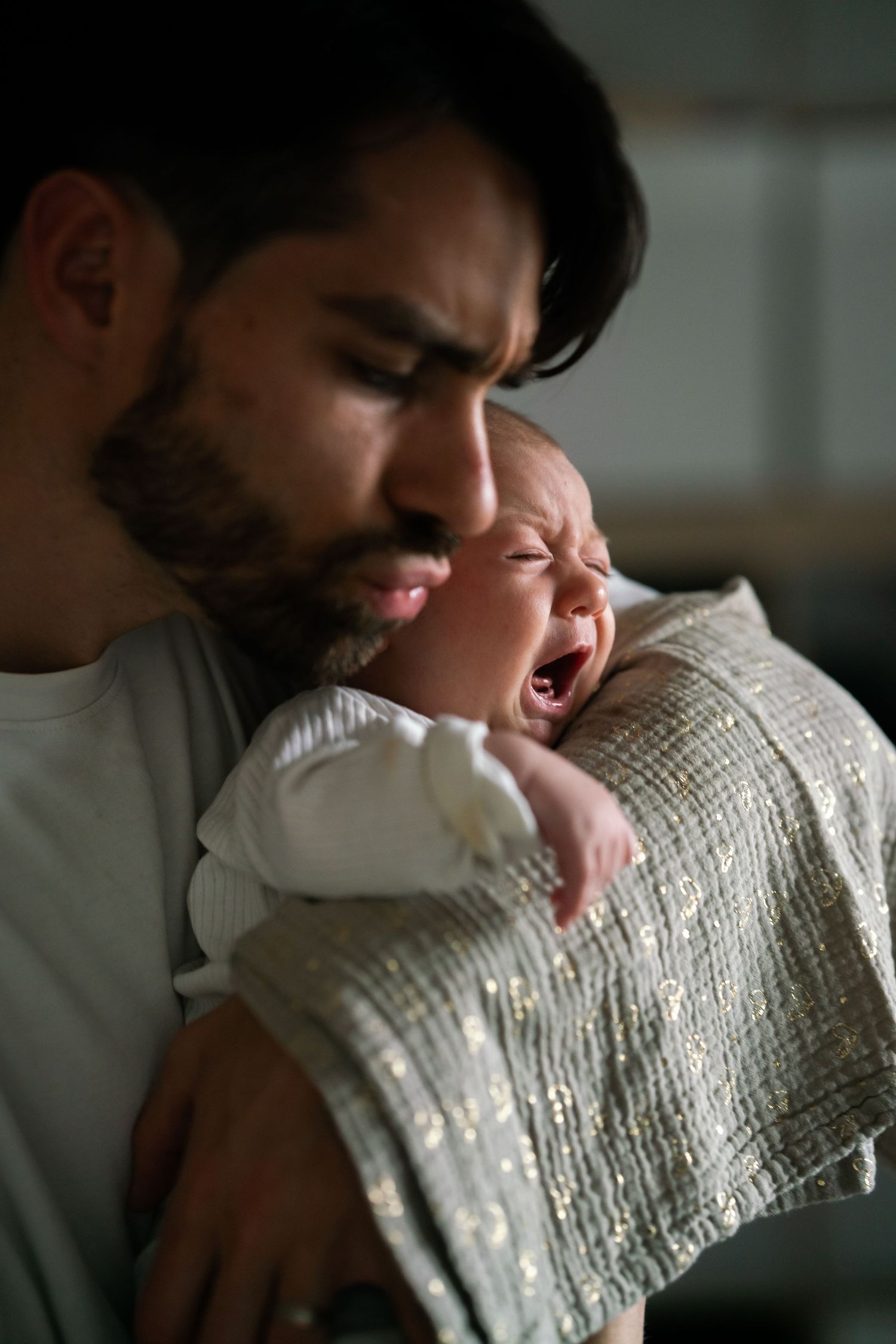 Close-up photograph of a father gently comforting his crying newborn baby in his arms at home.