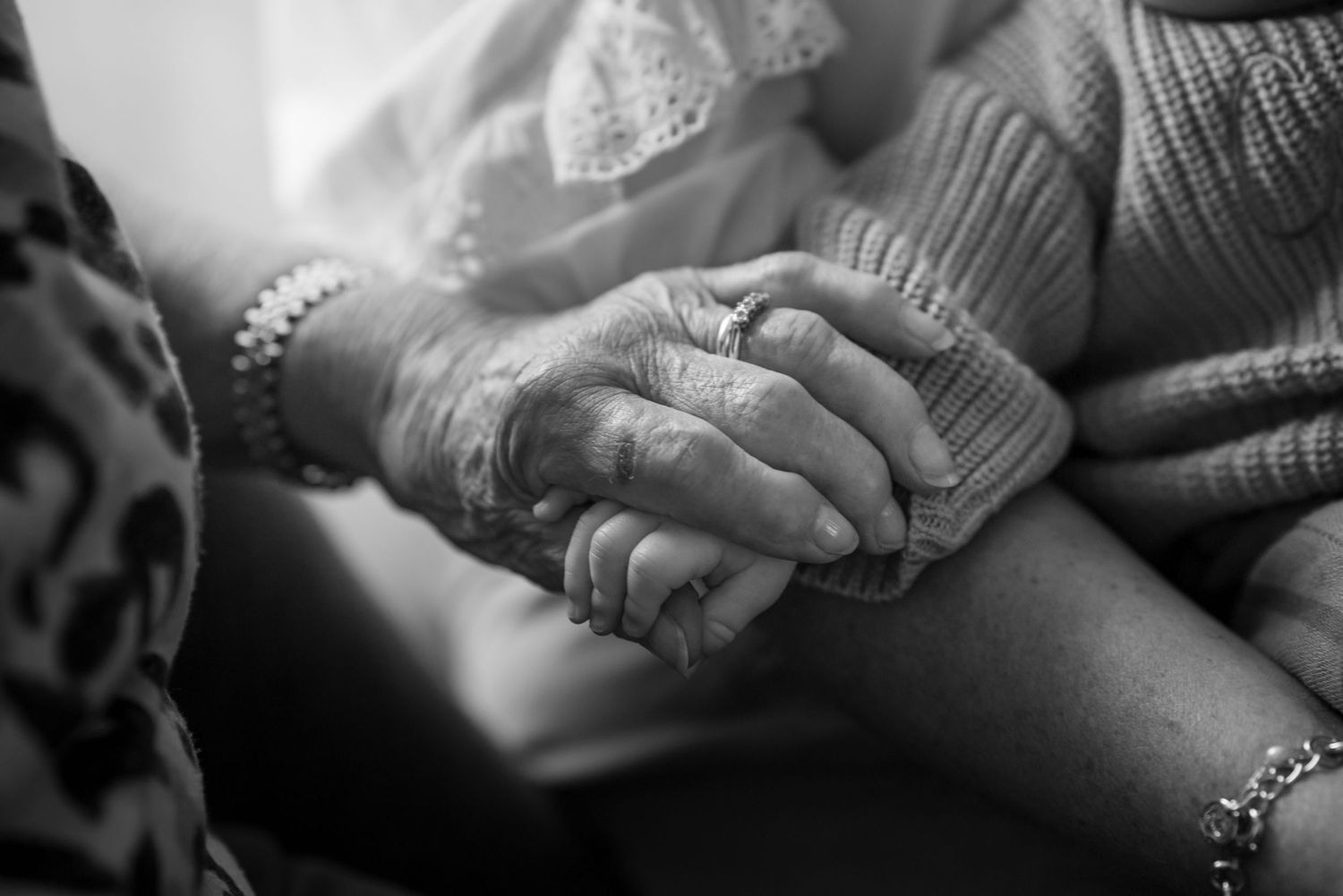 A black and white close-up of two elderly people gently holding hands together.
