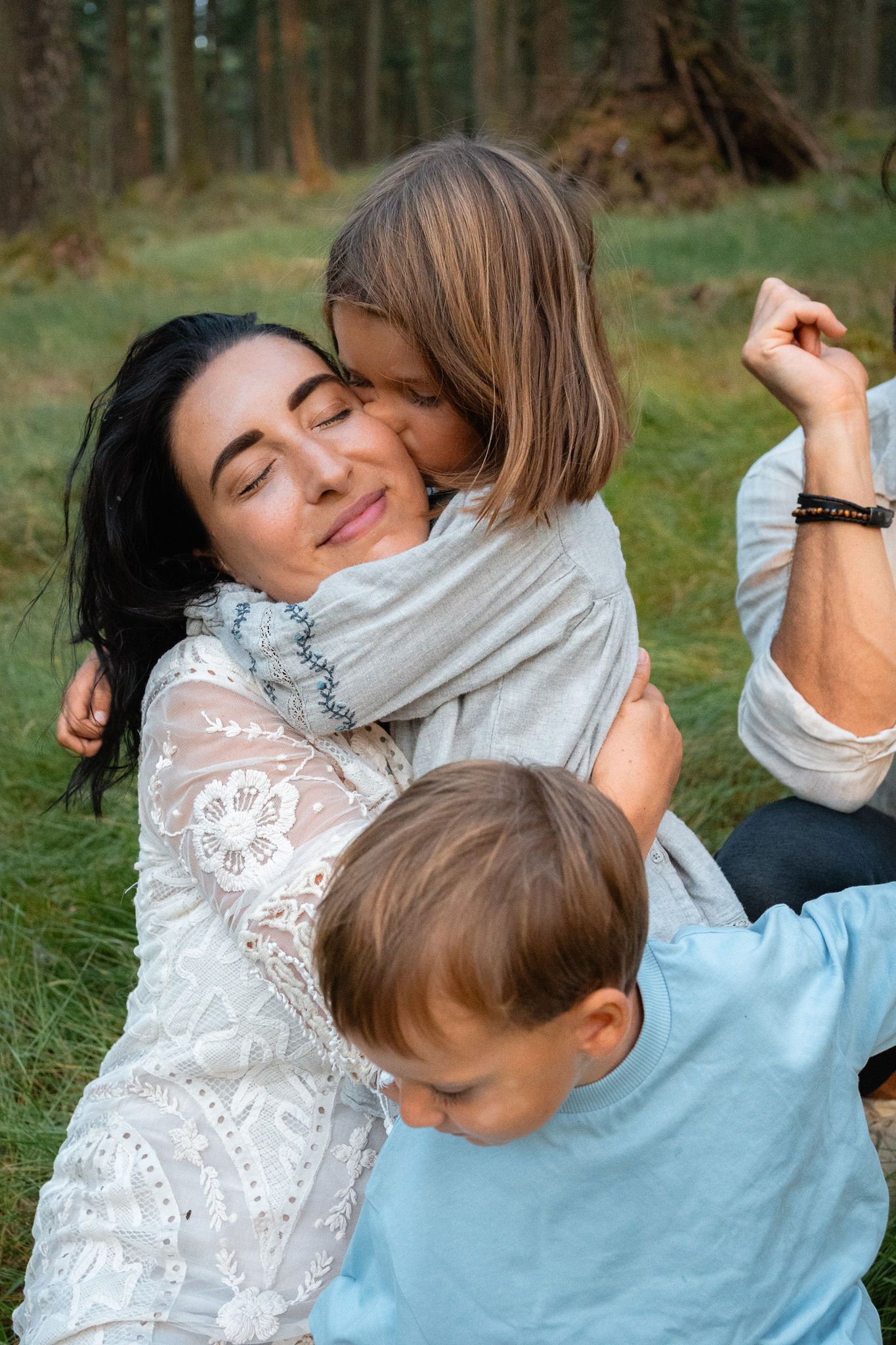 Maria Ryan-Kadem cuddling her daughter at home while her son jumps playfully nearby, photographed by @spiritandguts.