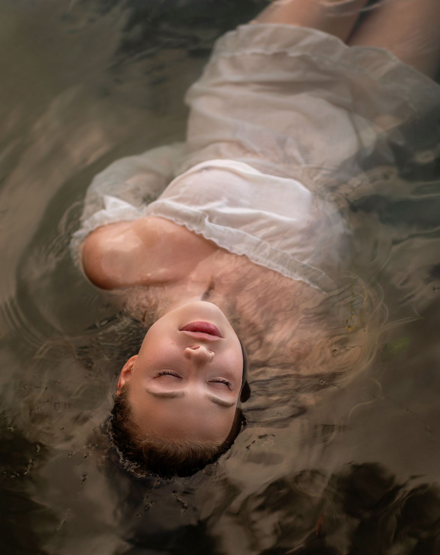 A serene woman in a white dress floating peacefully on calm water with eyes closed.
