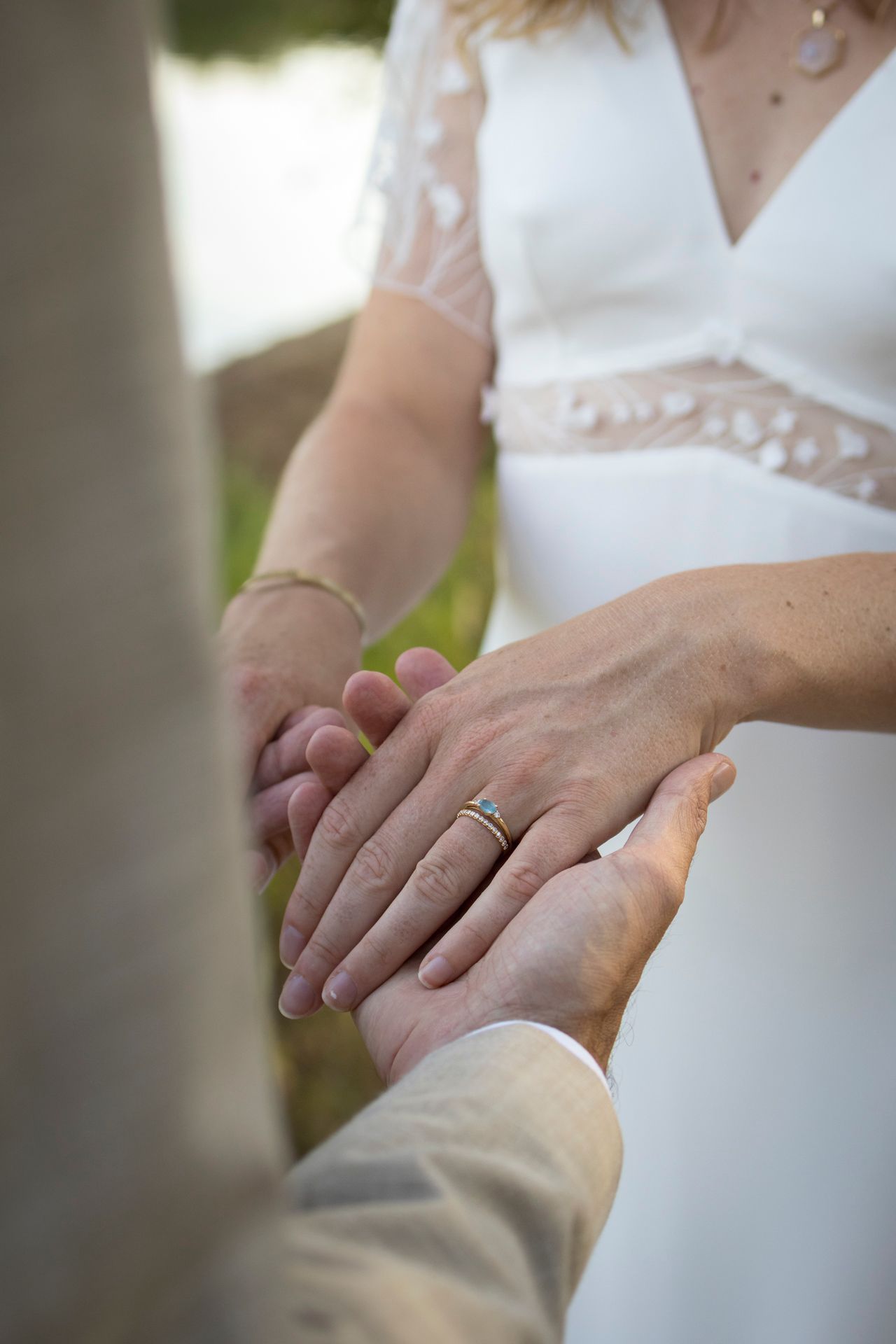 Gros plan sur les mains d’un couple qui se tiennent, mariée en robe blanche brodée, séance mariage à Lyon