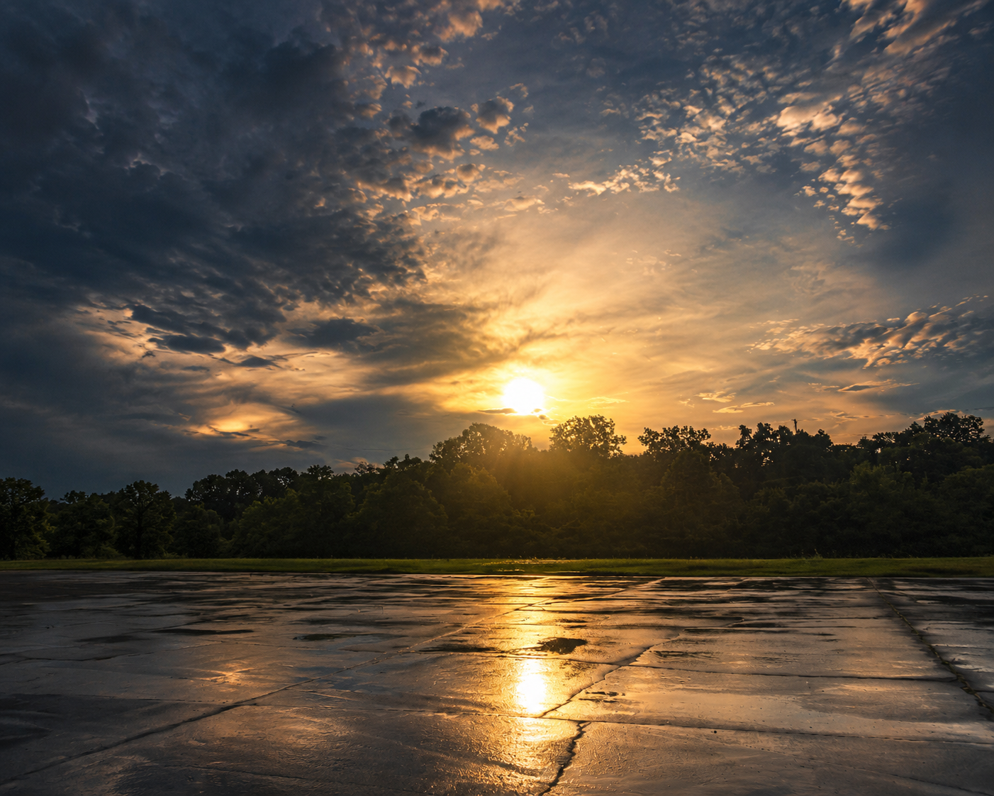 Golden sunset reflecting across wet pavement beneath a dramatic cloud-filled sky.