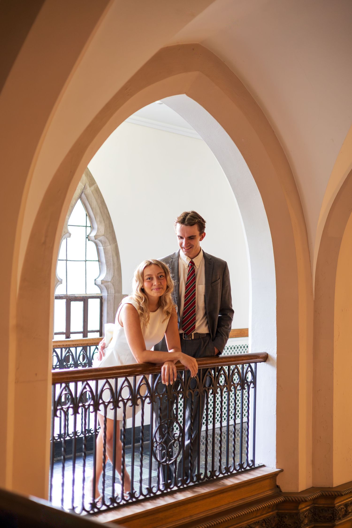 Elegant couple posing on ornate balcony with Gothic arches in a classic building interior.