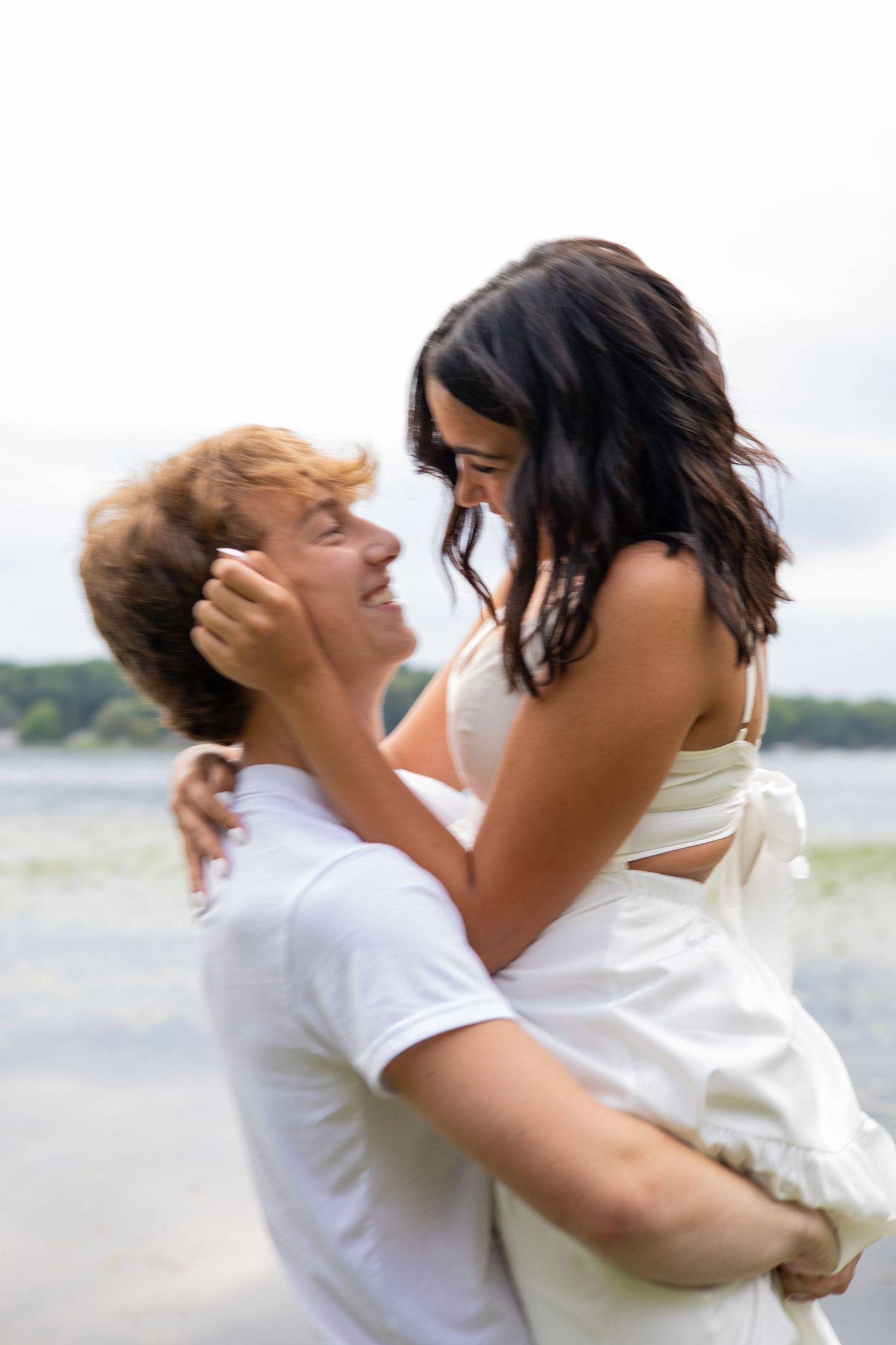 A couple shares a romantic moment on a beach, with the man lifting the woman in a white dress.