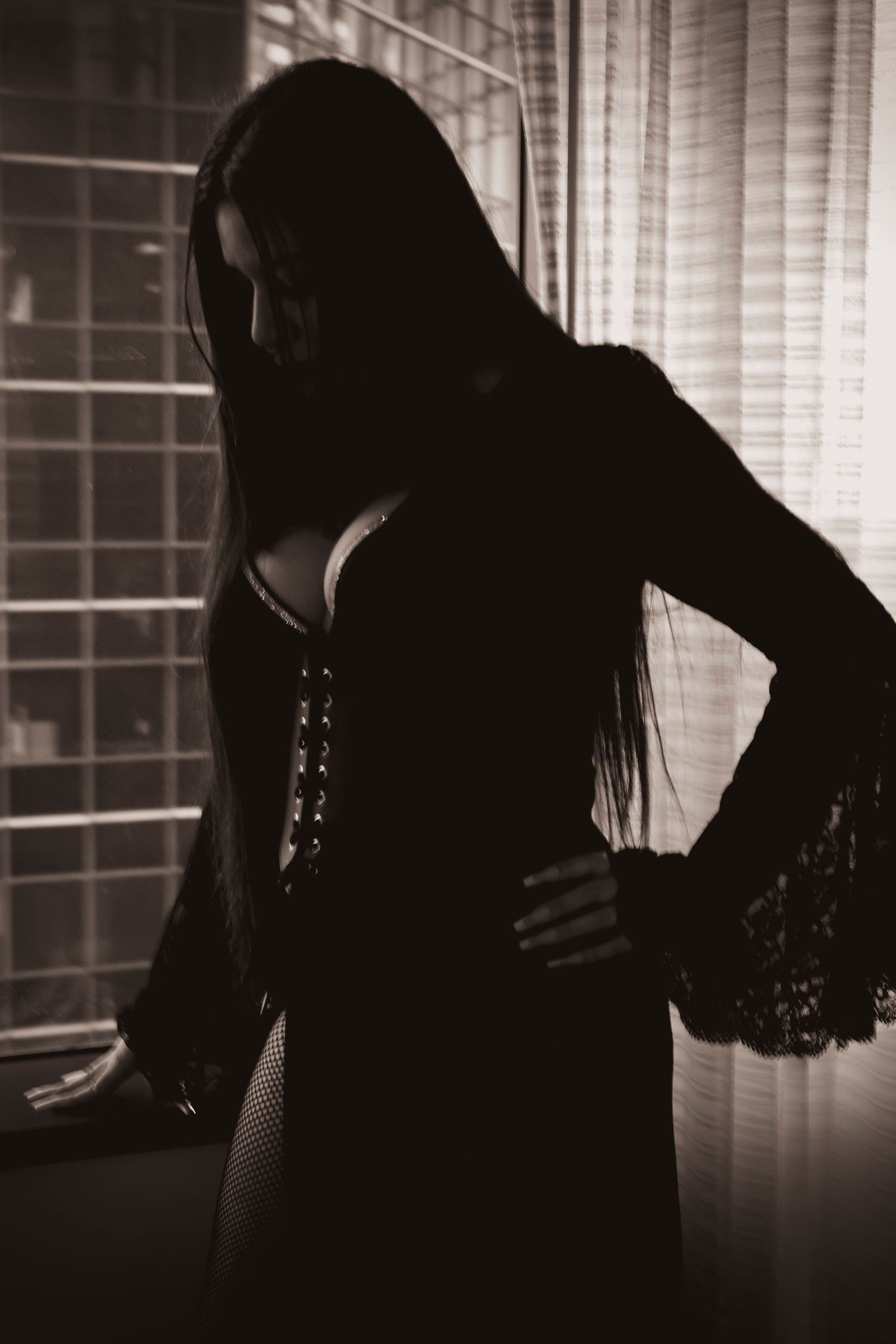Silhouette of a woman in black lace dress posing by a window in moody black and white.