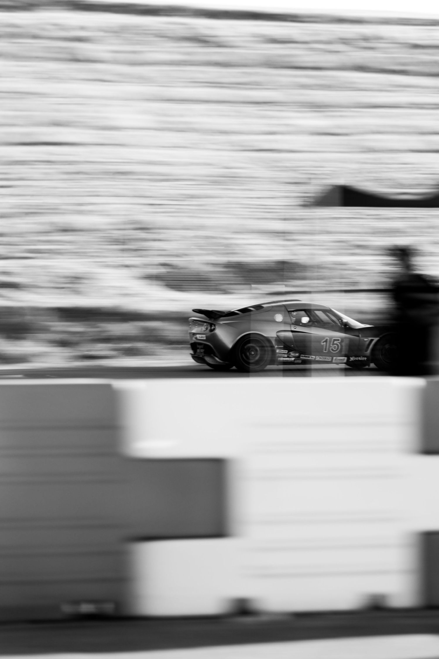 Black and white panning shot of a race car number 16 speeding past concrete barriers.