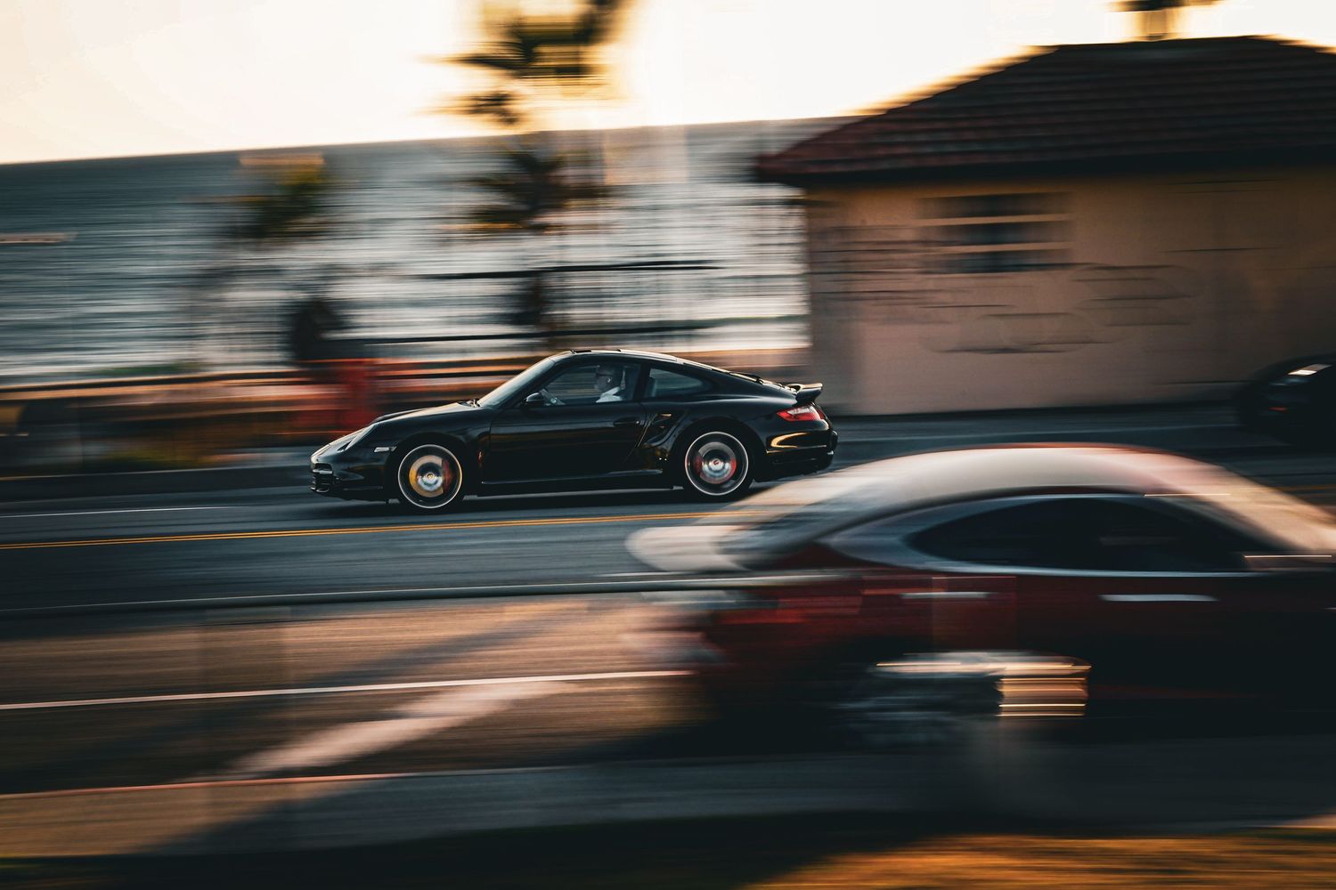 A sleek black Porsche speeds down a suburban street at golden hour, captured with motion blur.