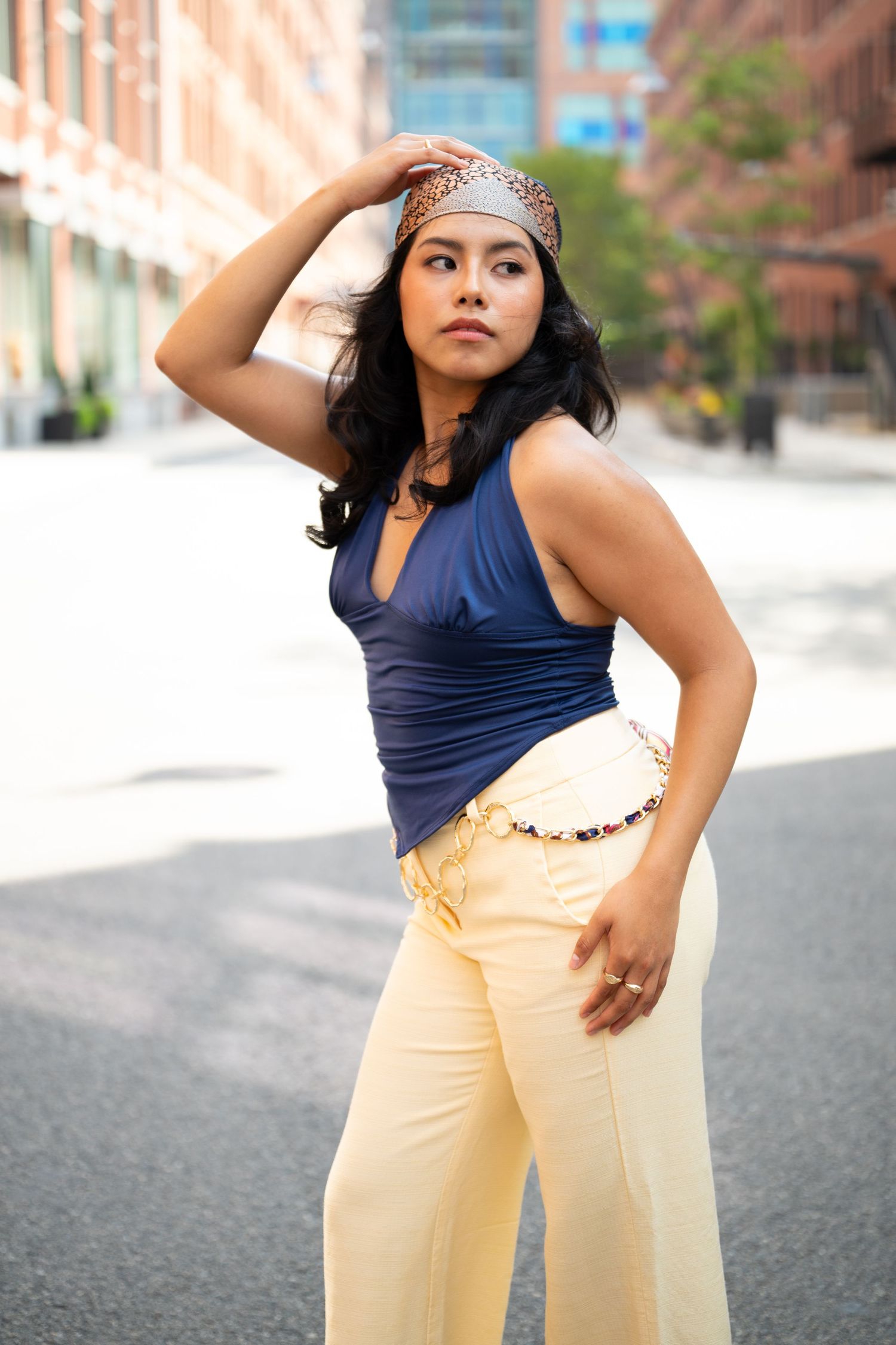 Woman in blue halter top and cream wide-leg pants poses dramatically on urban street.