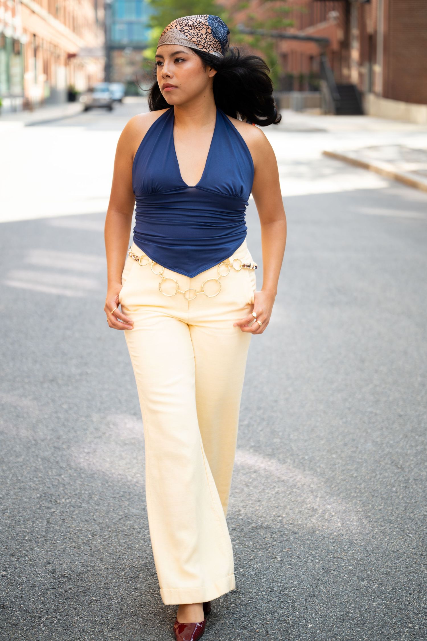 Fashion model walks confidently in blue halter top and cream flare pants on urban street.