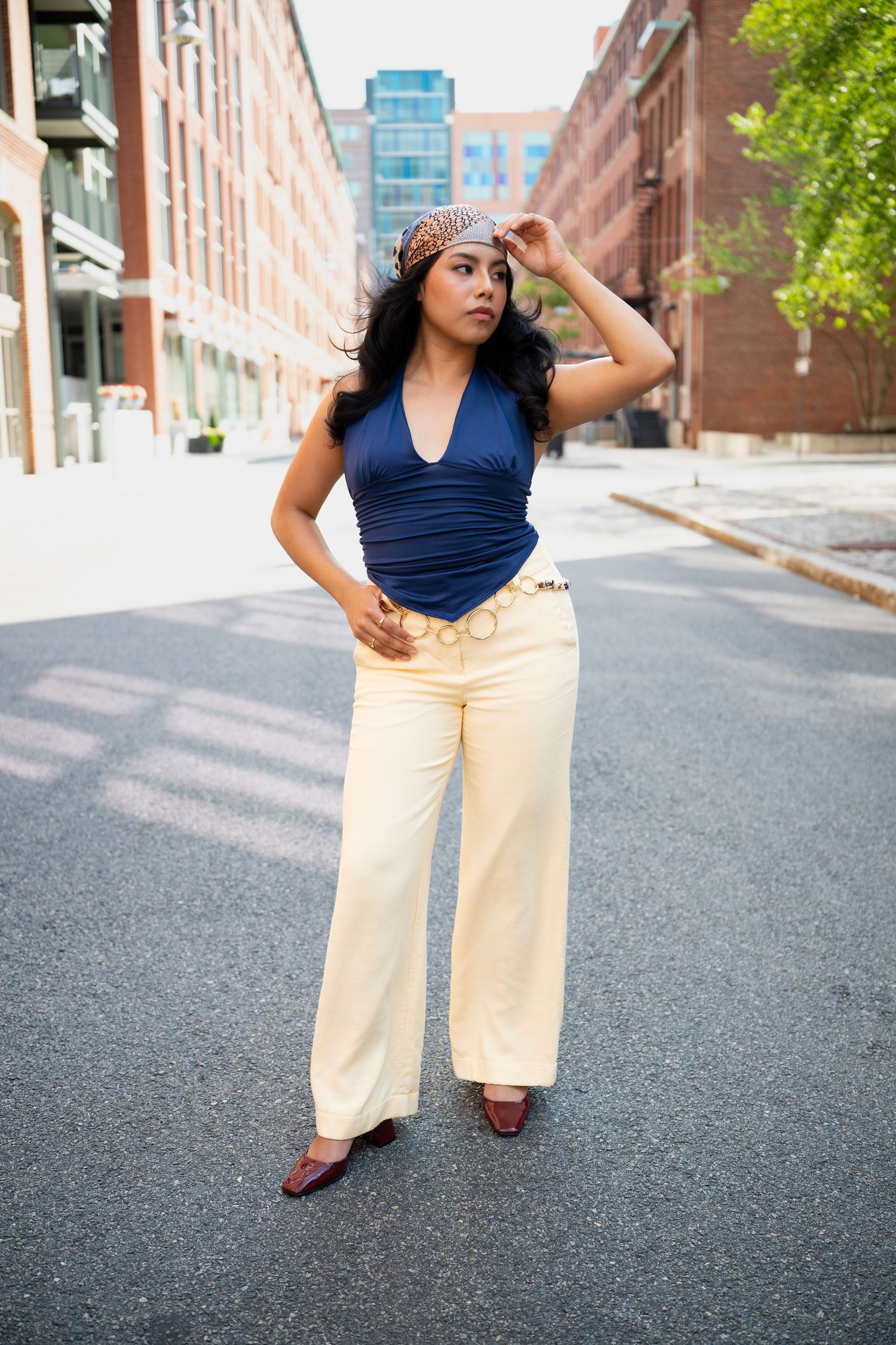 Woman in blue halter top, cream wide-leg pants, and leopard headband posing on urban street.
