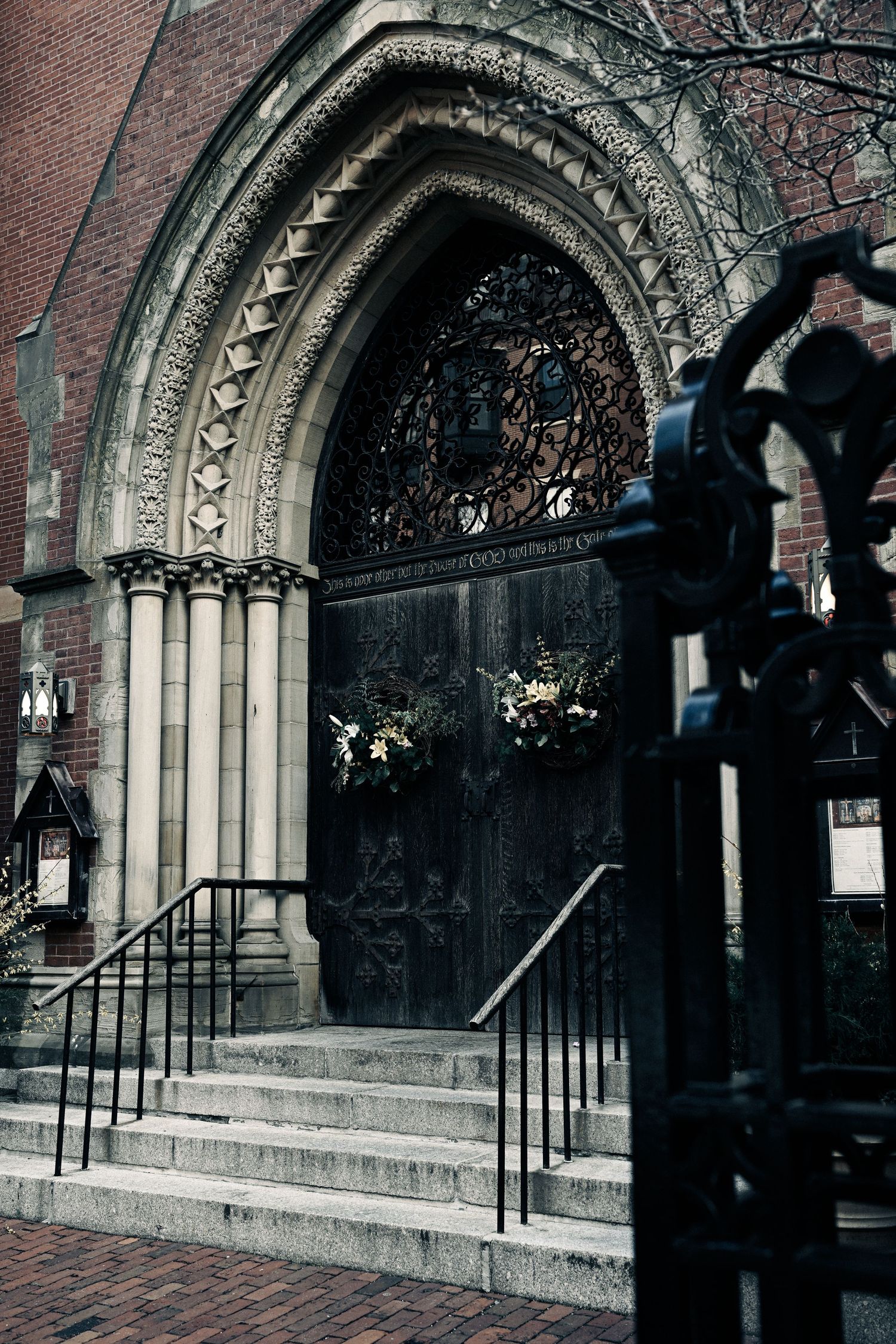 Gothic church entrance with ornate stone archway, decorative wrought iron gate, and holiday wreaths on dark wooden doors.