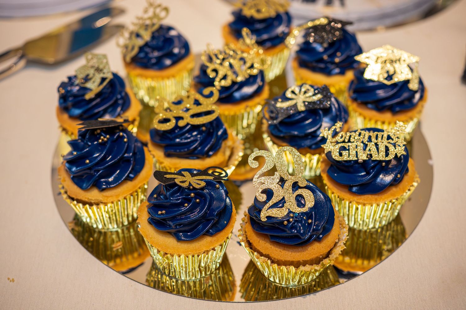 Blue and gold graduation cupcakes with Congrats Grad toppers and number 26 decorations on gold tray.
