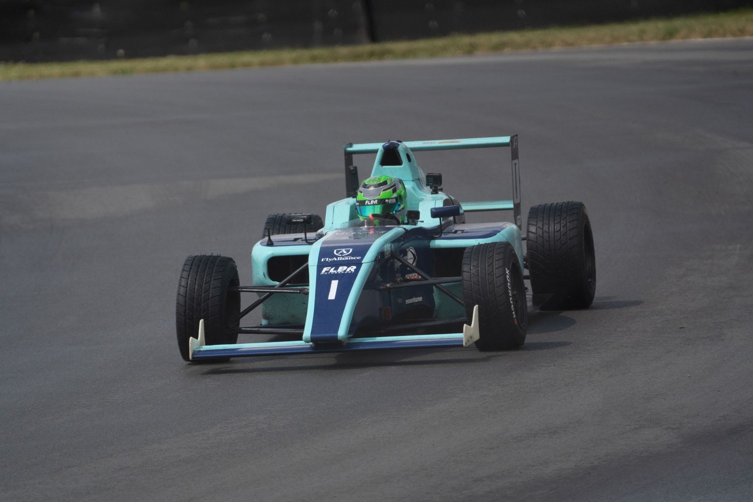 Green and white Formula 4 single-seater race car navigating a turn on a racing circuit.