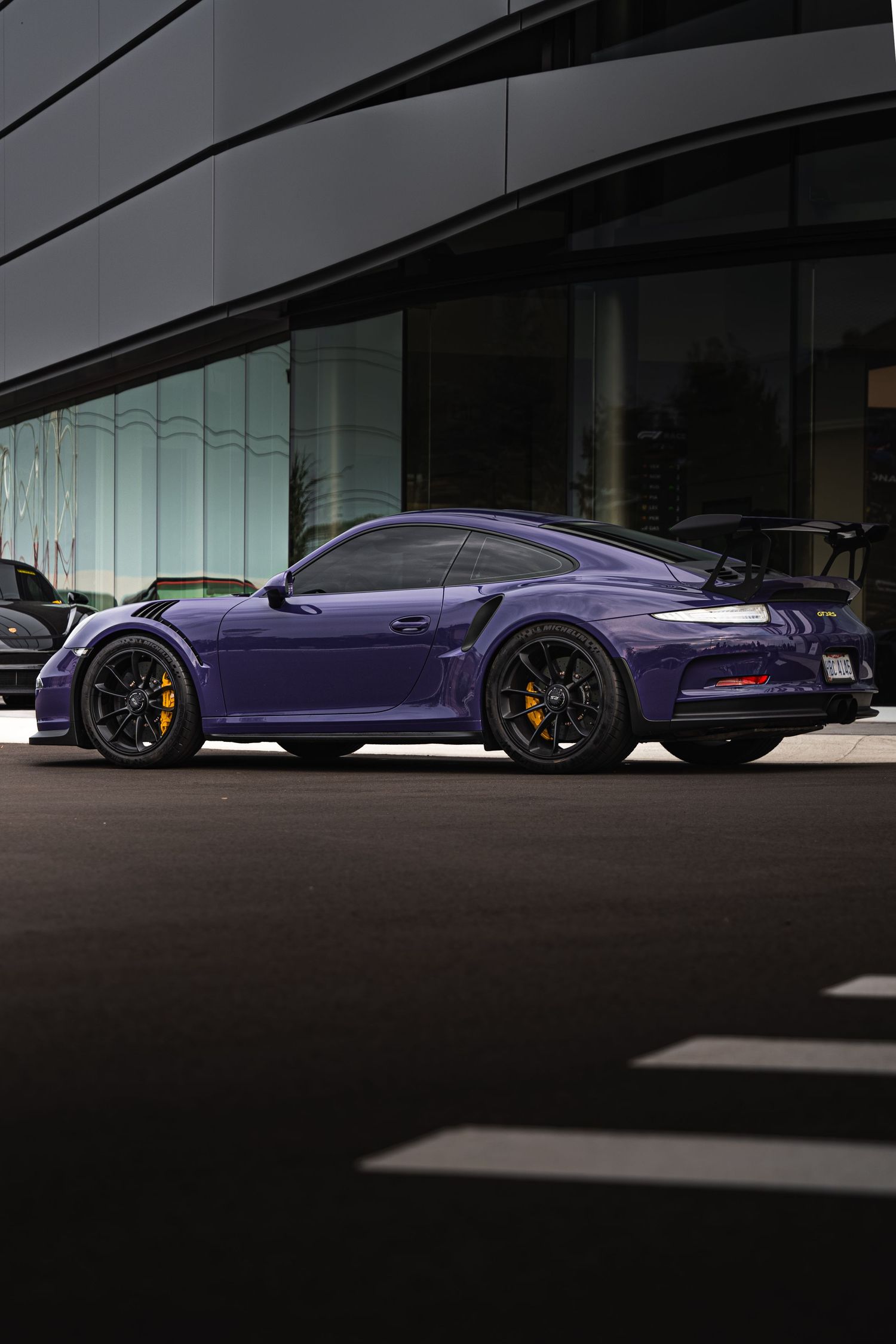 Ultraviolet purple Porsche 911 GT3 RS parked outside a modern glass building at dusk.