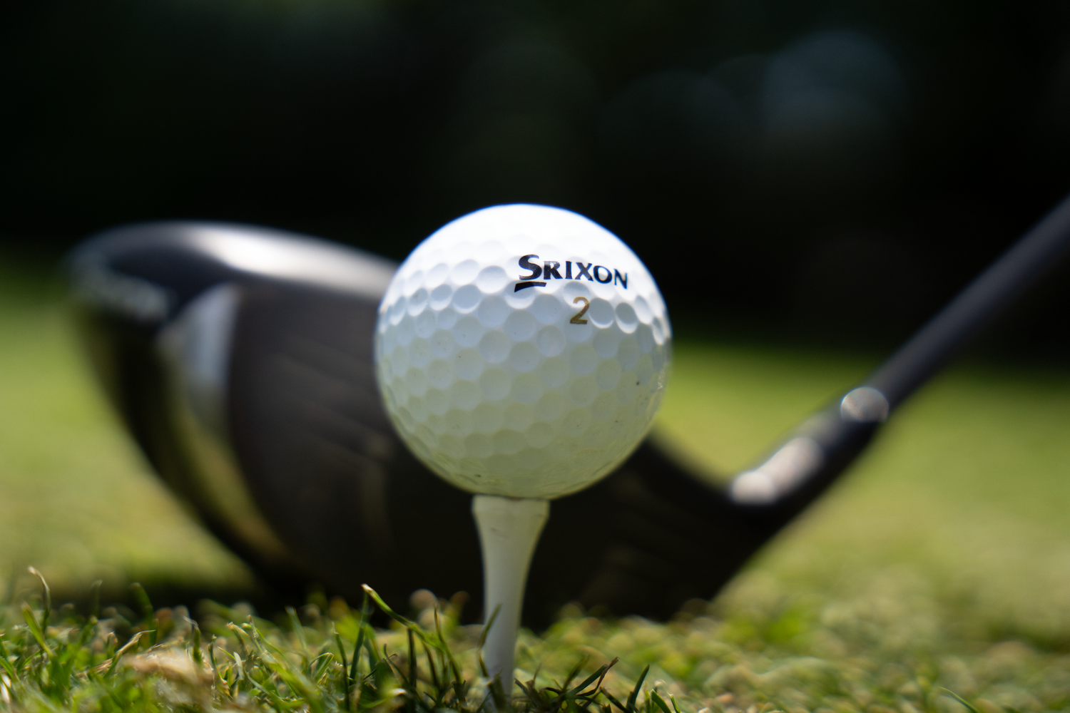 Srixon golf ball on a white tee with a driver club head in the background on a golf course.