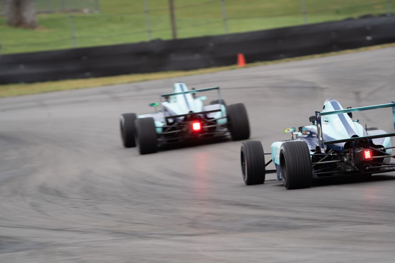Formula racing cars competing on a wet track during an open-wheel motorsport race event.