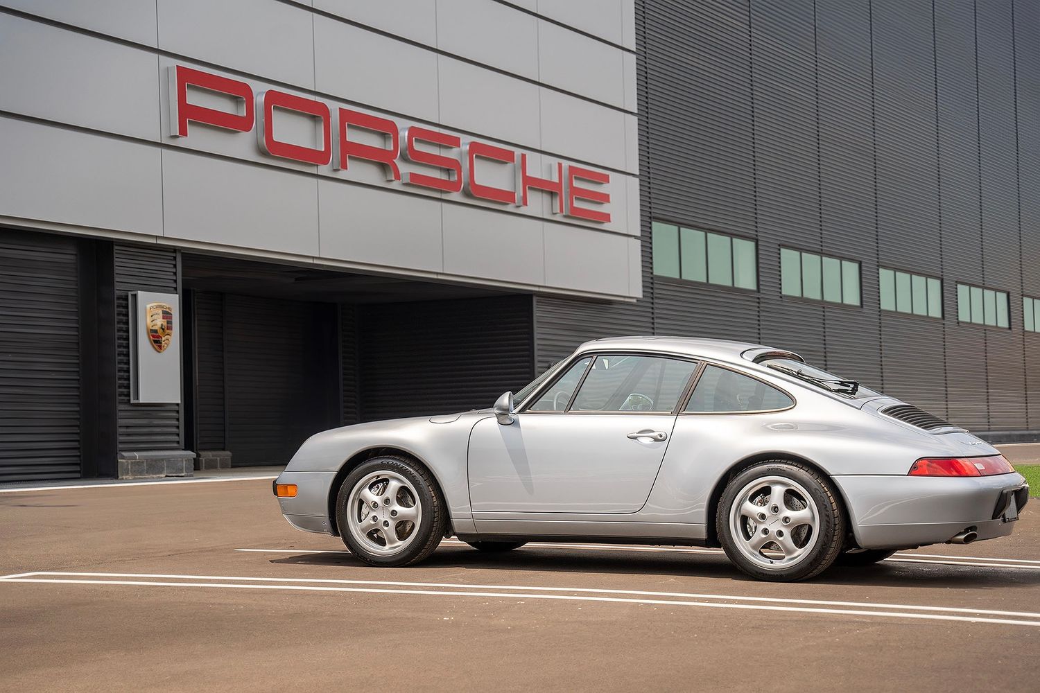 Classic silver Porsche 911 993 parked outside the official Porsche headquarters building.
