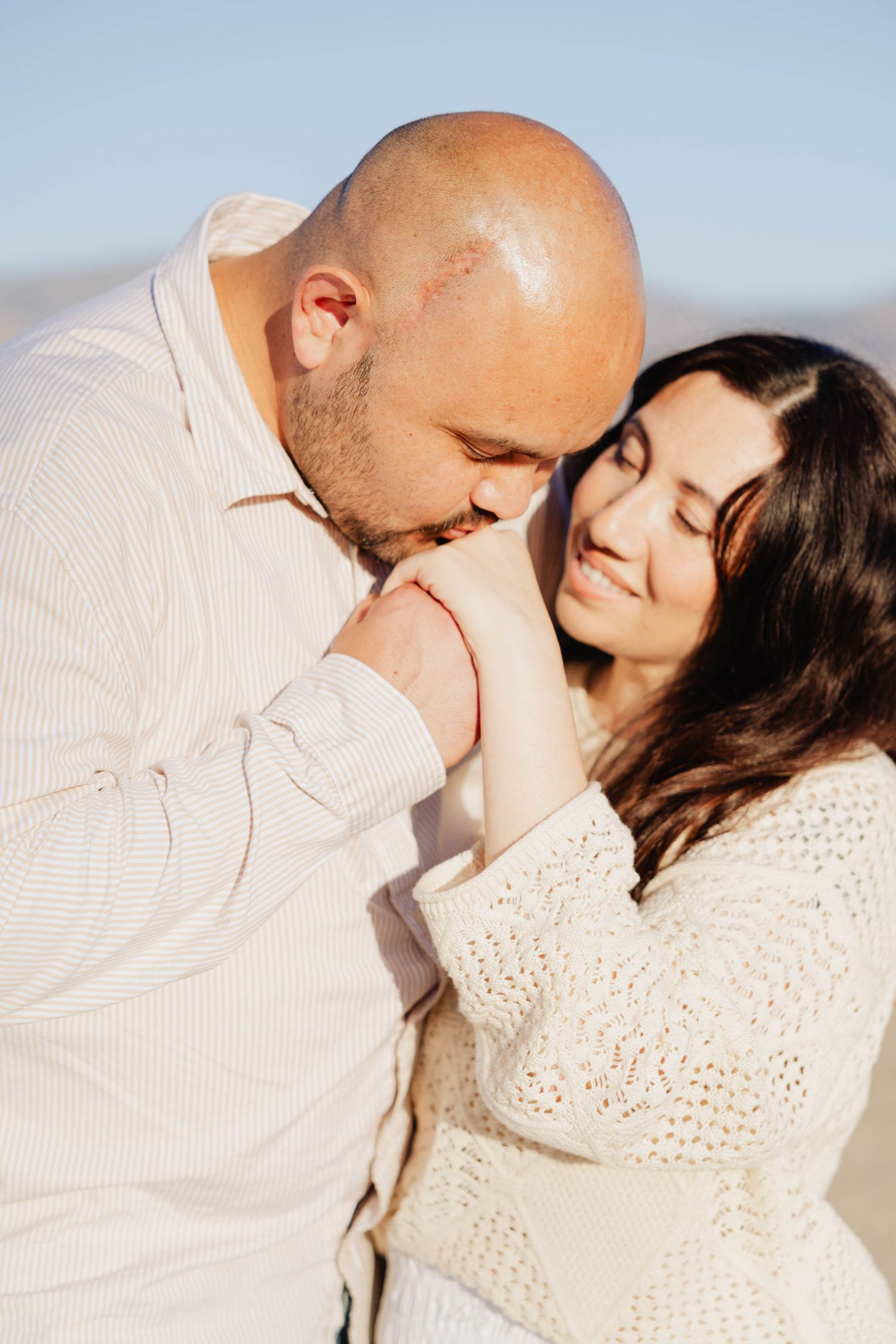 Husband kissing his wife’s hand while she smiles during a couples photo session in San Diego