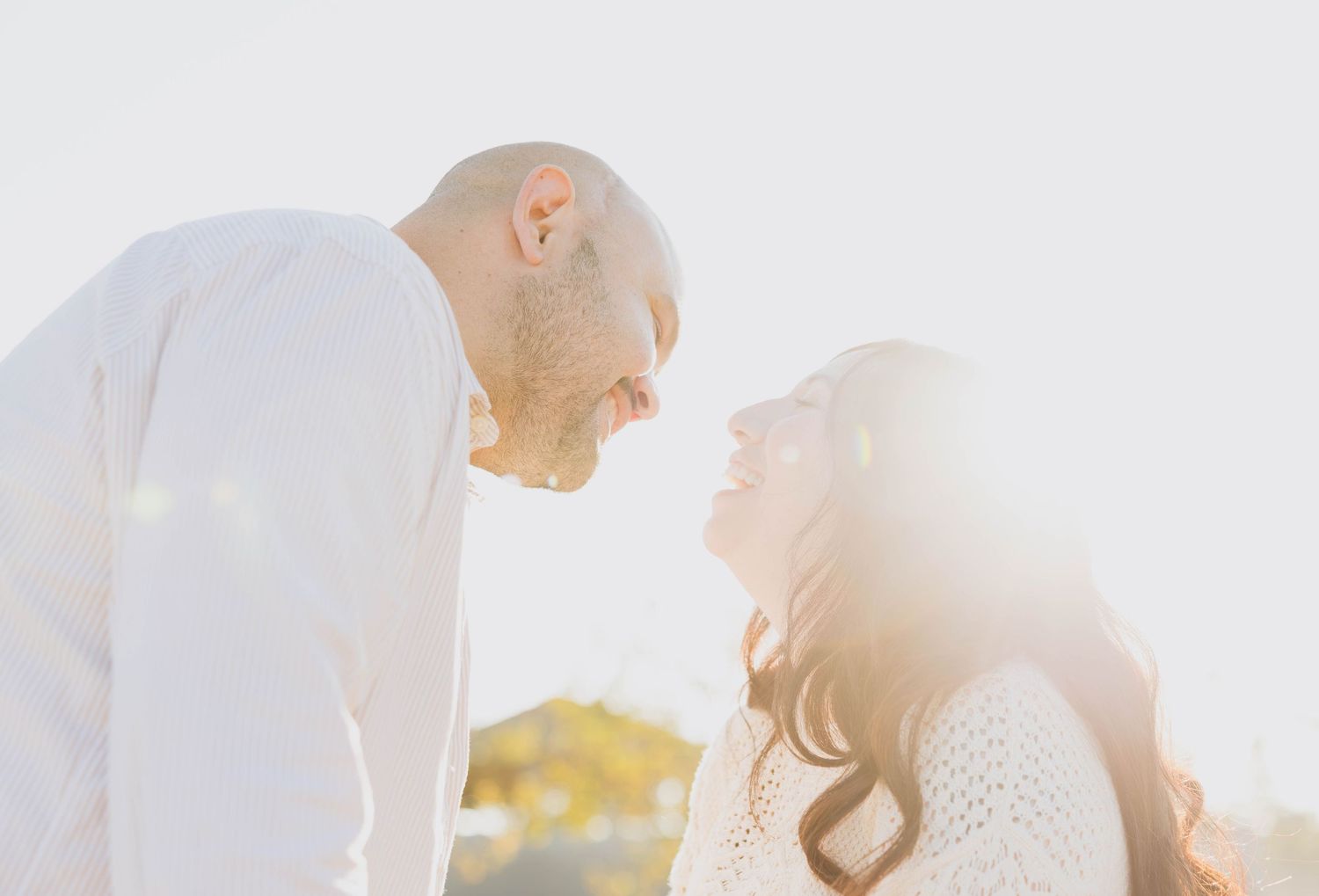 Couple leaning in for a kiss and smiling in warm backlight during a San Diego couples session
