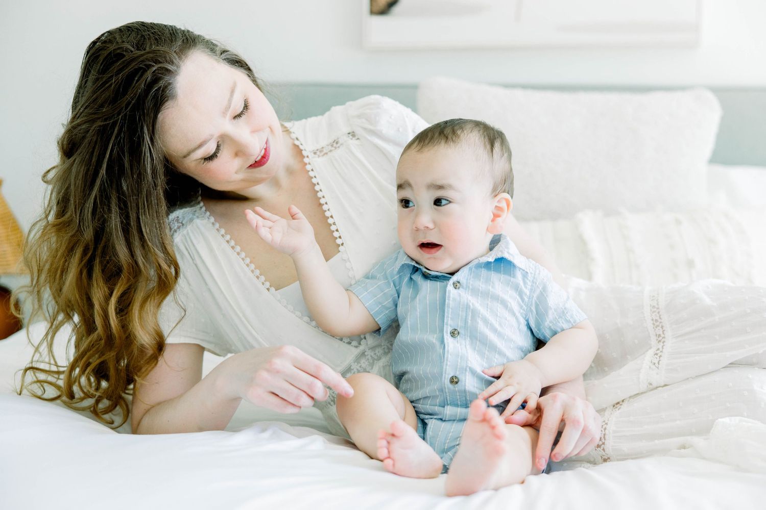 Mother and baby playing together on a cozy white bed during a motherhood photoshoot in San Diego