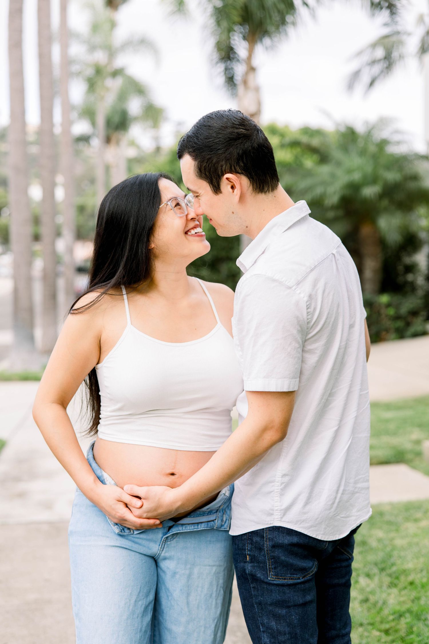 Expecting couple touching noses and smiling while holding the baby bump during an outdoor maternity photoshoot