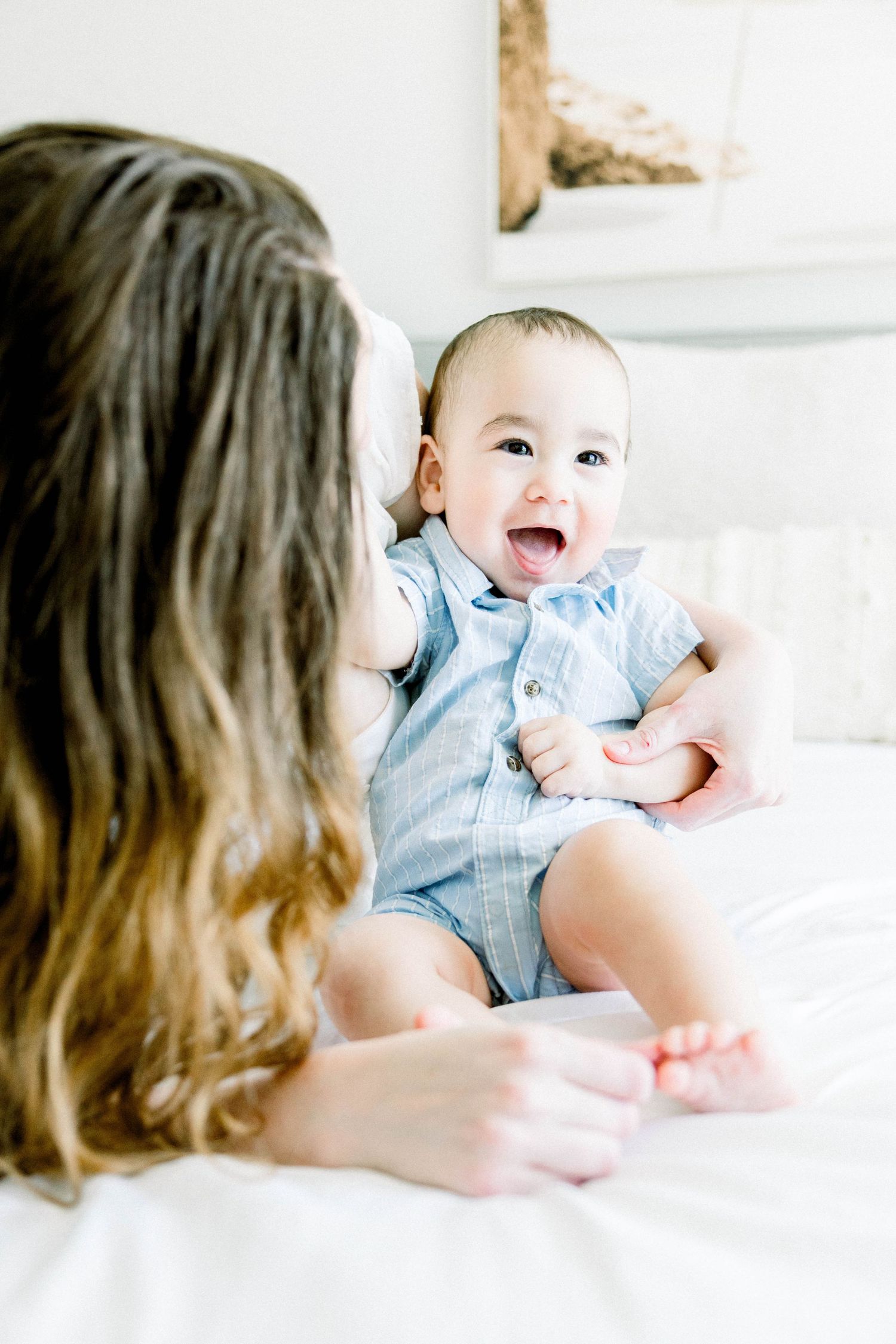 Baby giggling while sitting on a bed next to his mother during a San Diego lifestyle motherhood session