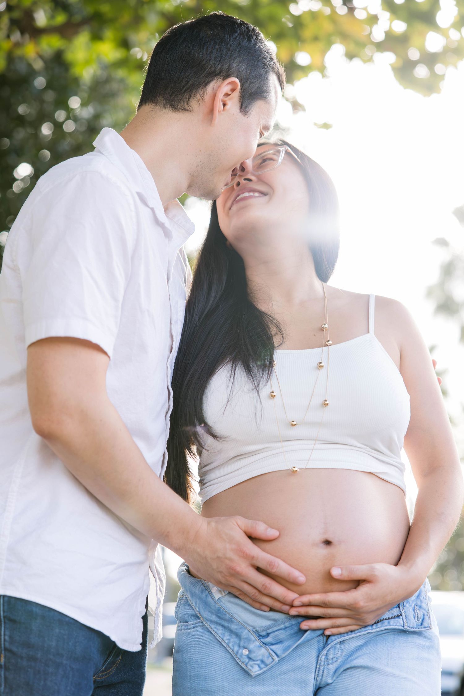 Husband kissing his pregnant wife as they hold her baby bump together during a San Diego maternity session