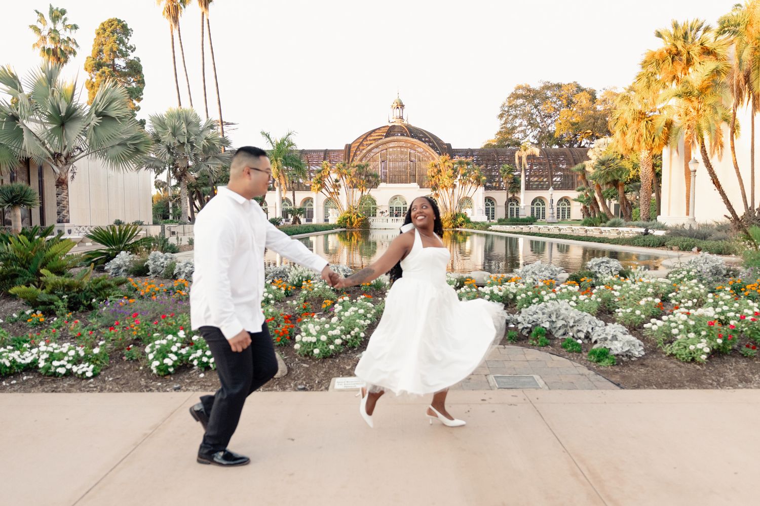 Couple holding hands and walking past a flower garden and reflecting pool in San Diego