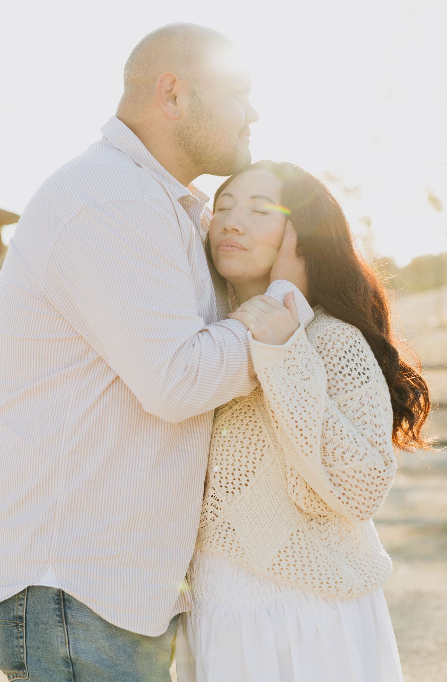 Man kissing his wife’s forehead as she closes her eyes in a warm embrace during a San Diego couples session