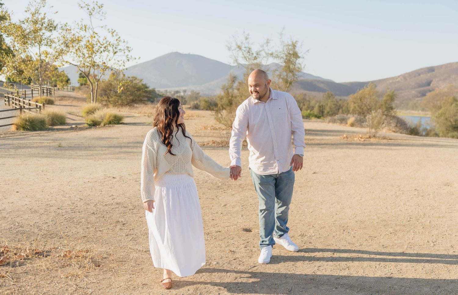 Couple walking toward the camera hand in hand on a dirt trail with hills in the background during a San Diego couples session