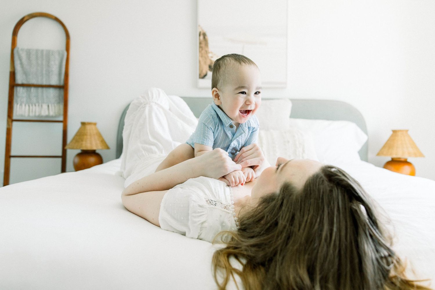 Mother lying back on the bed lifting her smiling baby above her during an in-home motherhood photoshoot in San Diego