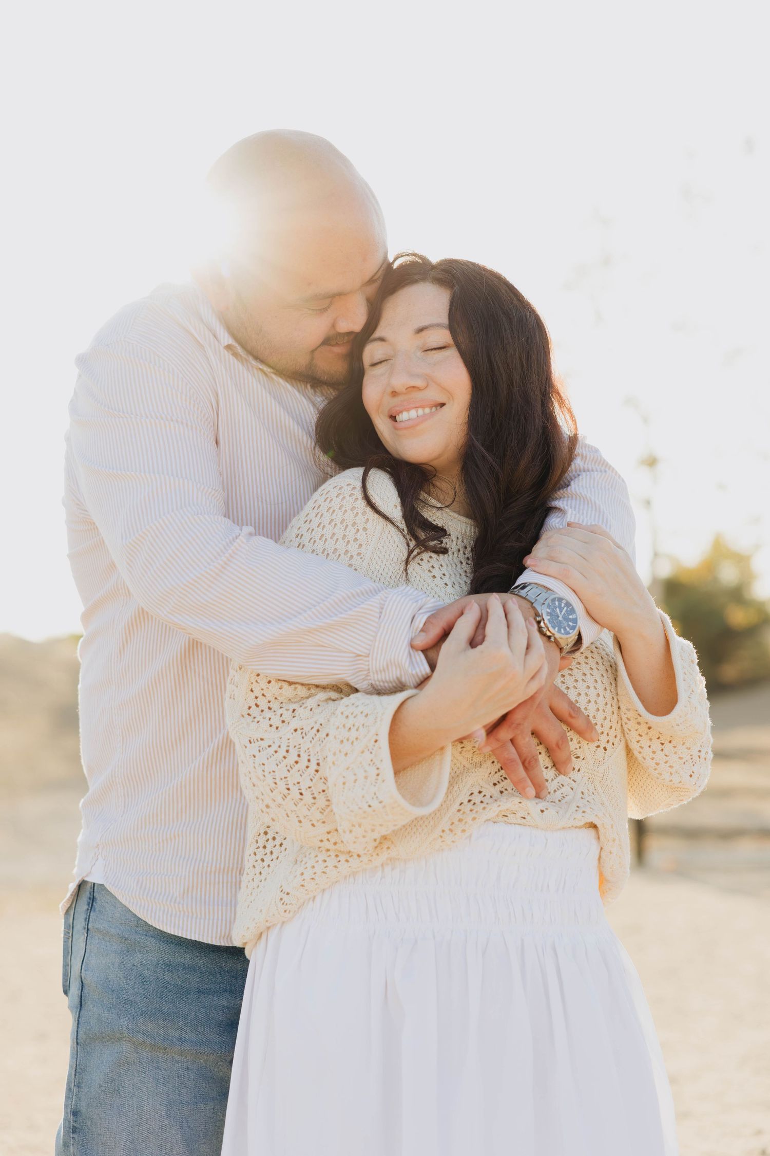 Smiling woman wrapped in her husband’s arms in golden light during a San Diego couples photoshoot