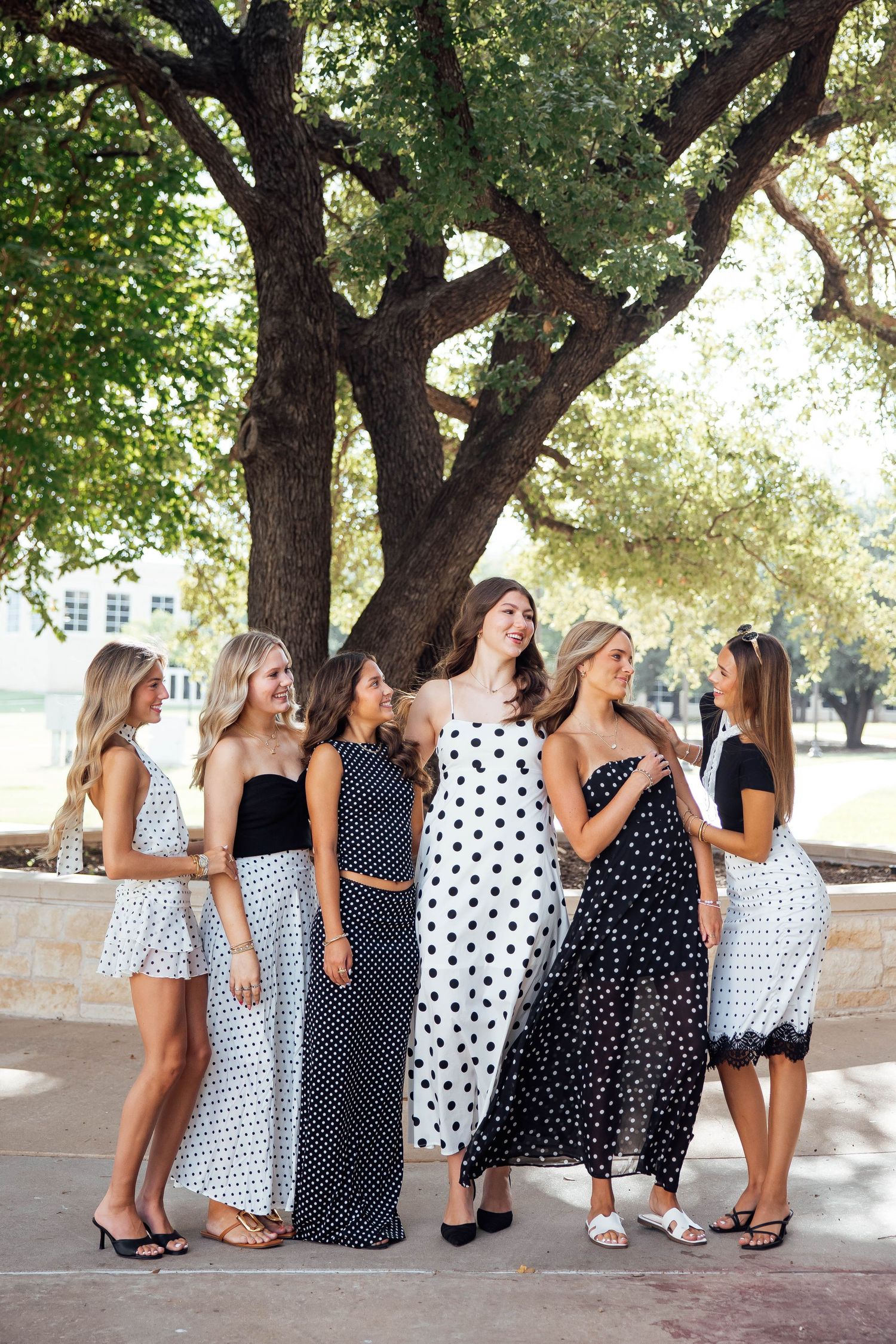 Group of six young women in black and white polka dot outfits posing under a large oak tree.