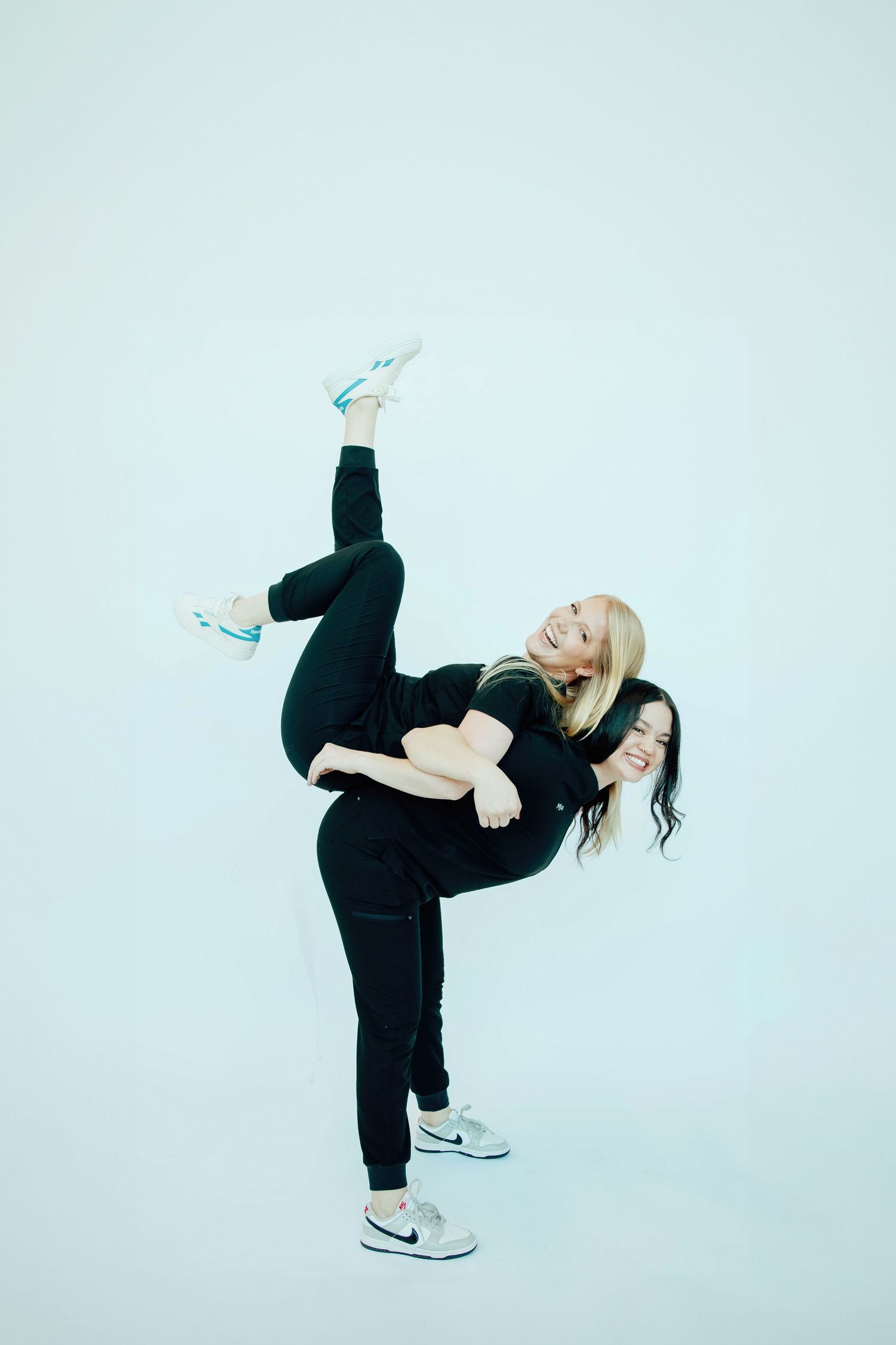 Two women in black outfits playfully posing together against a light background.
