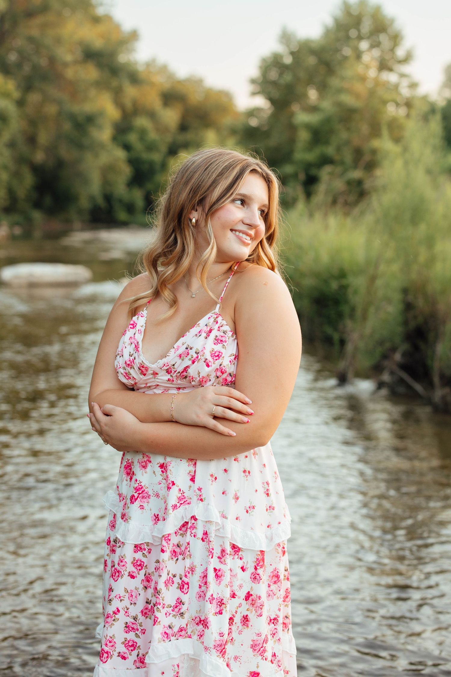 Smiling blonde young woman in floral dress standing by a peaceful river with green reeds.