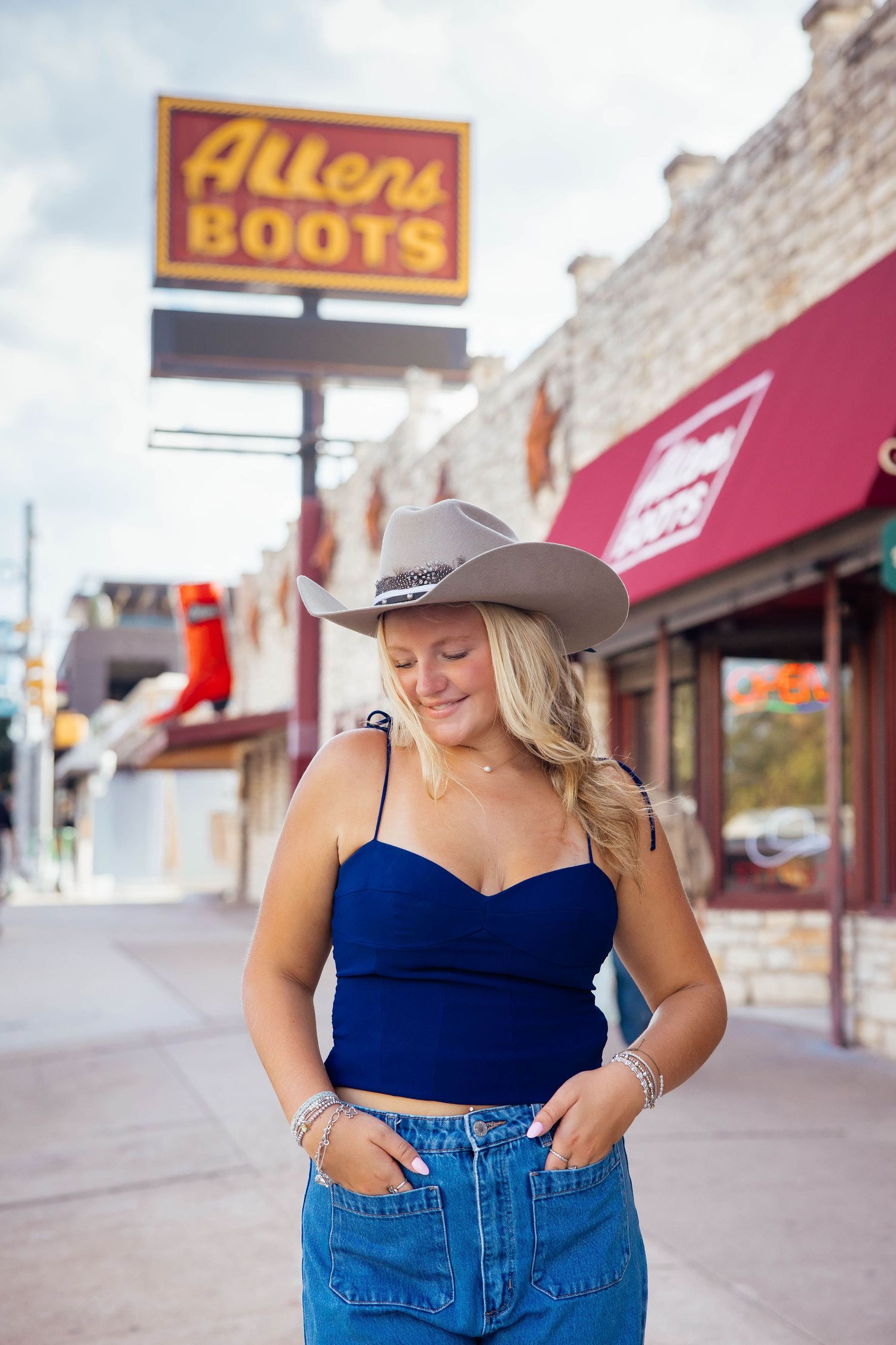 Blonde woman in blue crop top and jeans wearing cowboy hat outside Allen's Boots store in Austin.