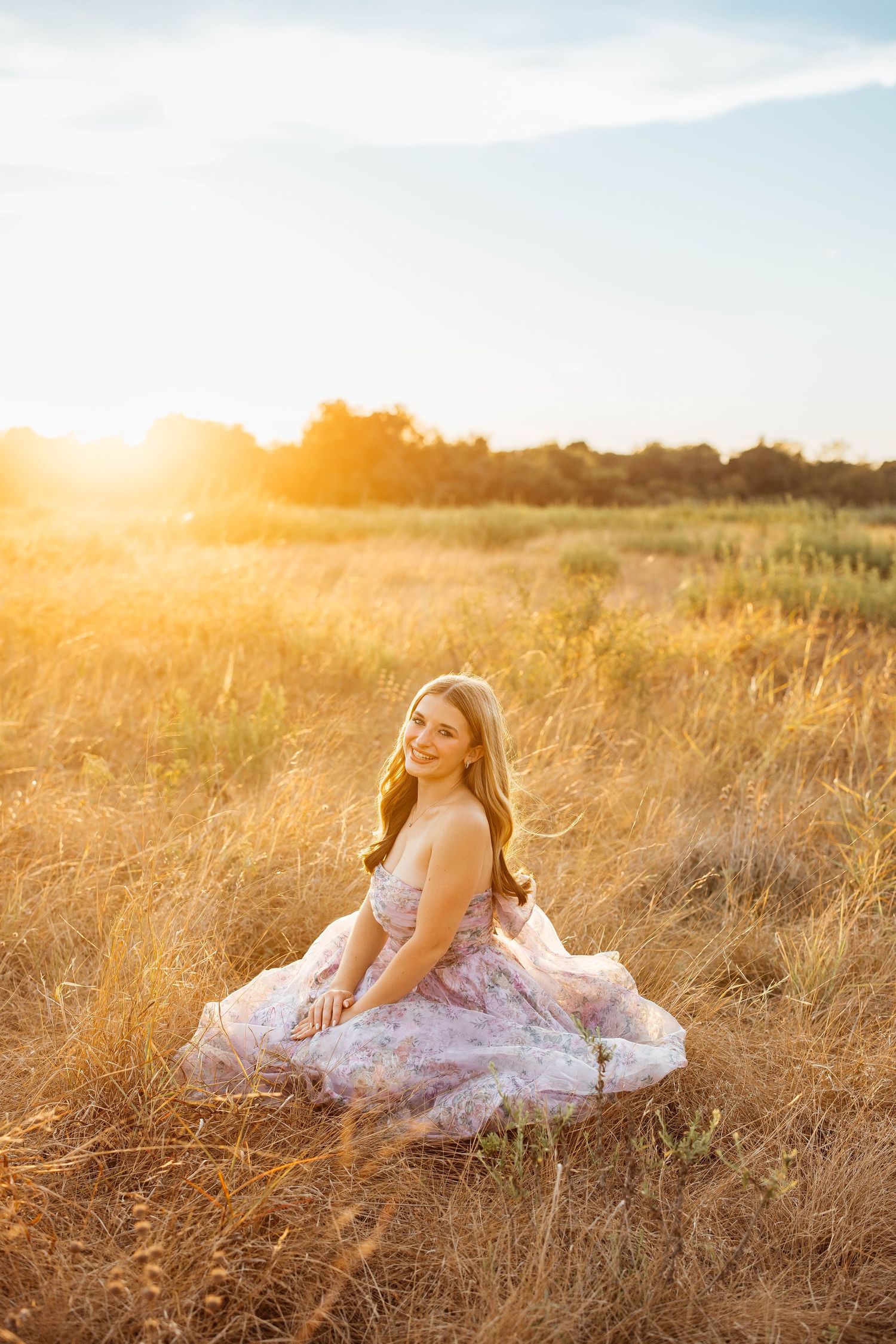 Young woman in floral dress sitting in golden field at sunset.