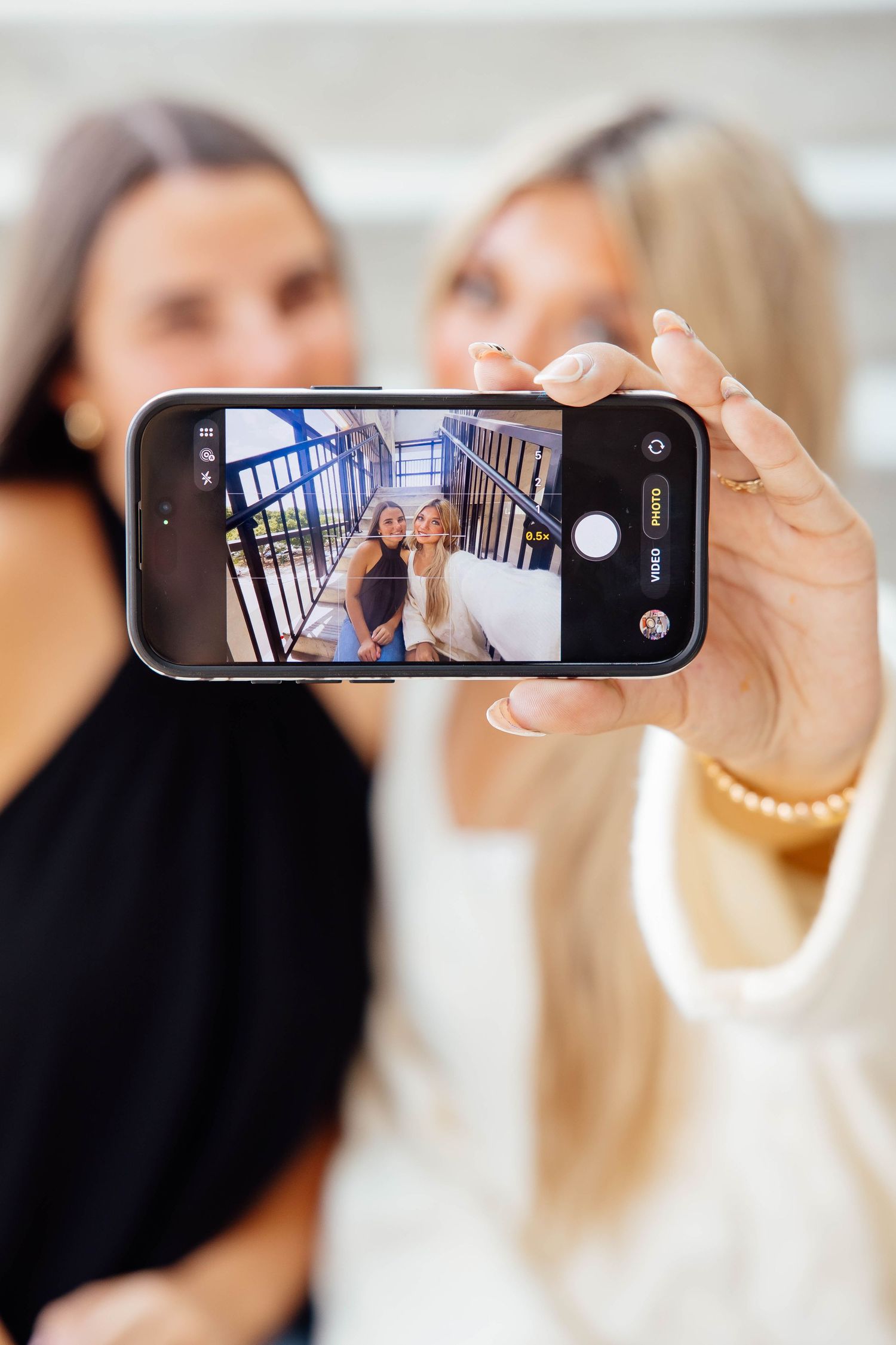 Two women taking a selfie on a phone showing them posed on a staircase.