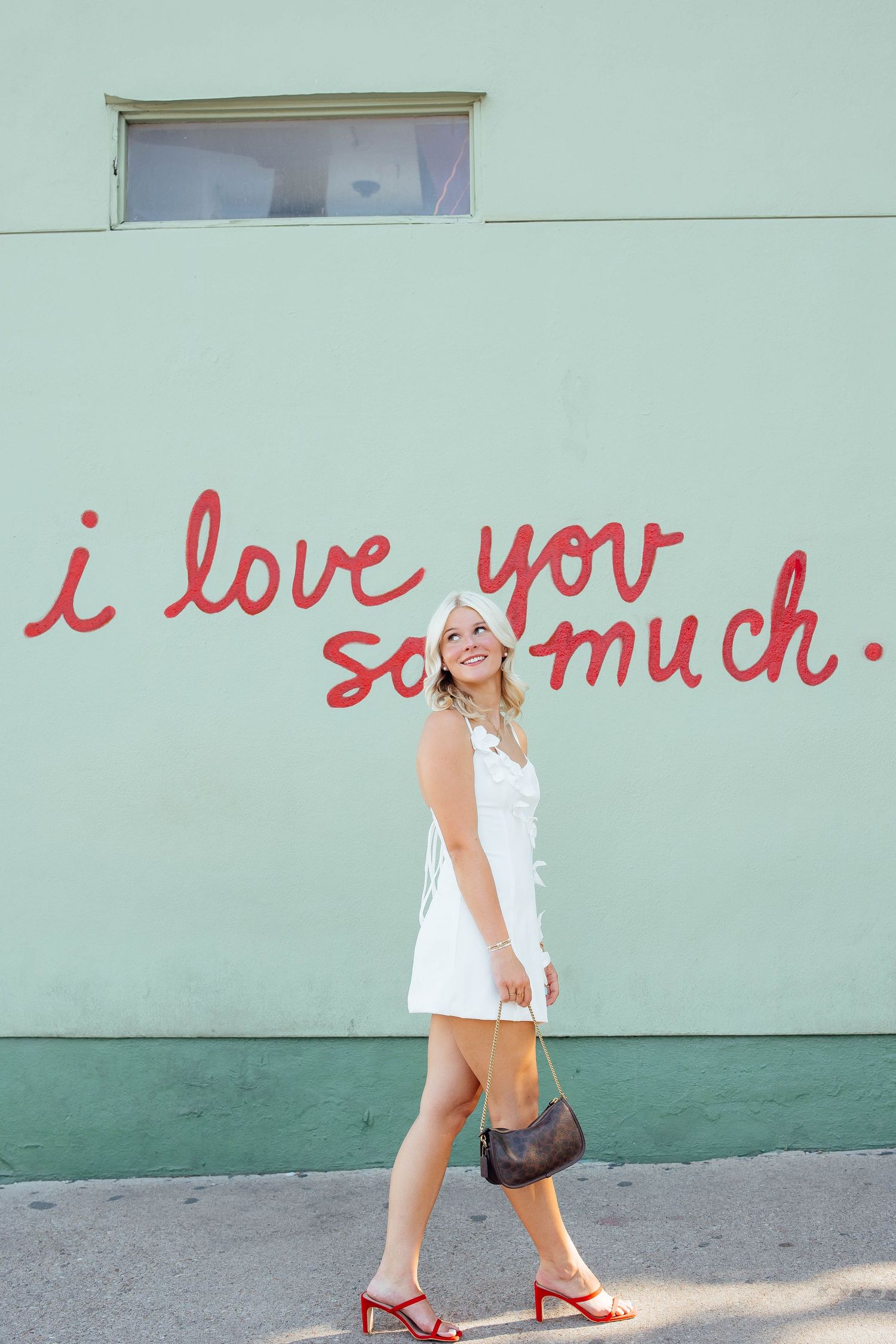 Blonde woman in white mini dress walks past iconic i love you so much mural in Austin TX.