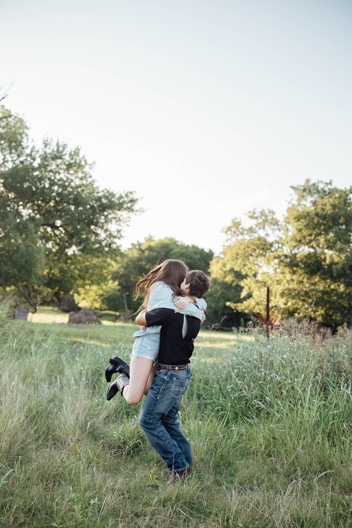 Young couple embracing and kissing in a green grassy field at sunset.